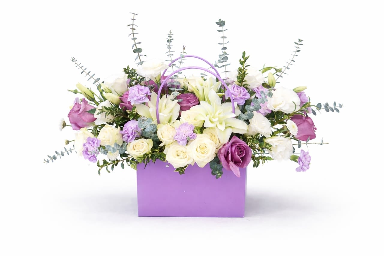 Lavender Bag of Flowers - Soft lavender and white blooms spill from a lavender gift bag to create a romantic birthday bouquet or thoughtful just-because arrangement that feels both fresh and celebratory. This gift-bag presentation-perfect for birthdays, anniversaries, or a heartfelt thank-you-pairs creamy white lilies and roses with lavender and deeper purple roses and carnations, so the person you're thinking of will feel gently cherished the moment they see it.  