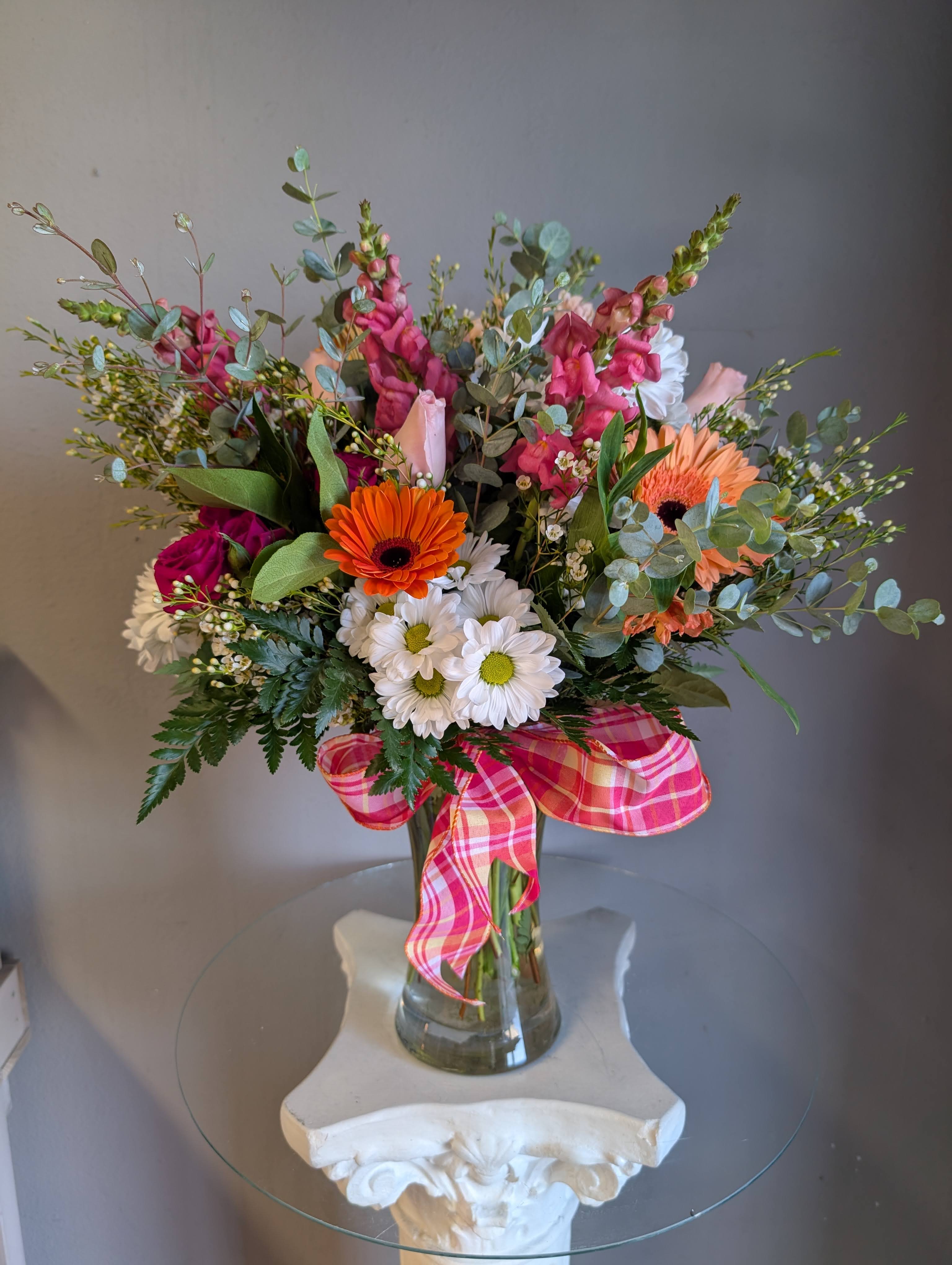 MDA #207 Mother's Day - Bright gerbera daisies and soft pink roses create an immediate pop of color in this garden-style flower arrangement, perfect as a Mother's Day bouquet. The mix of snapdragons, daisies, and leafy green branching stems gives the design a lively, airy silhouette that reads as joyful and feminine-the kind of bouquet that makes the person you're thinking of feel genuinely celebrated.  ***PLEASE NOTE*** 1) Please be flexible. Based on quality and/or availability substitutions of equal or greater value may be made at the designer’s discretion (including flowers, greens, filler, vase and hard goods) without notice. 2) BLOOMSNAPS AND TIMED DELIVERY ARE NOT AVAILABLE THE WEEKEND OF 5/7 - 5/10 3) Storefront will be open. Please check Google for special hours.