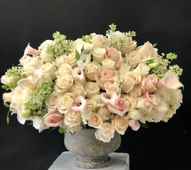 Large bouquet of cream and blush roses with calla lilies in a stone vase
