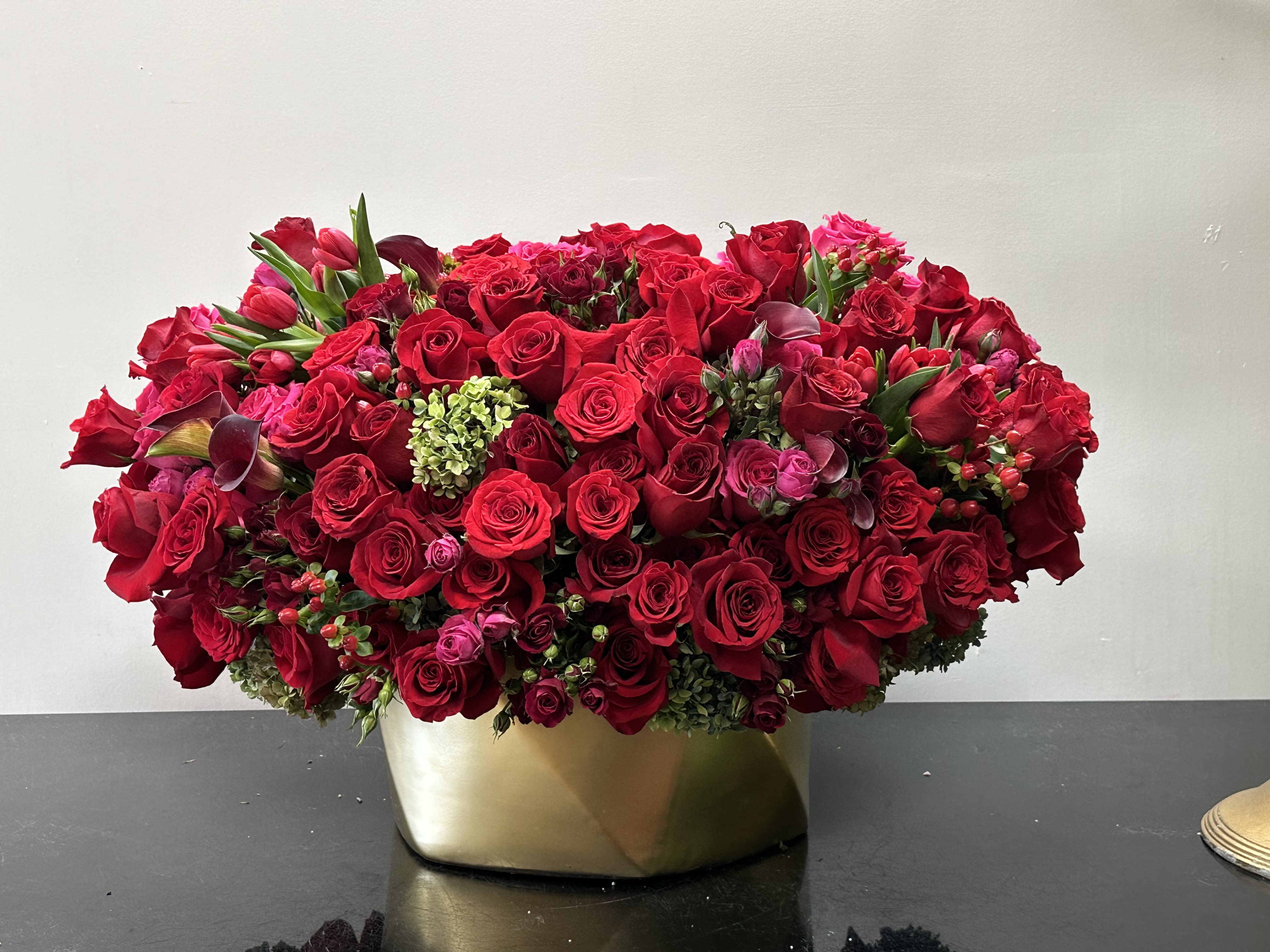Dense red rose arrangement in a gold vase