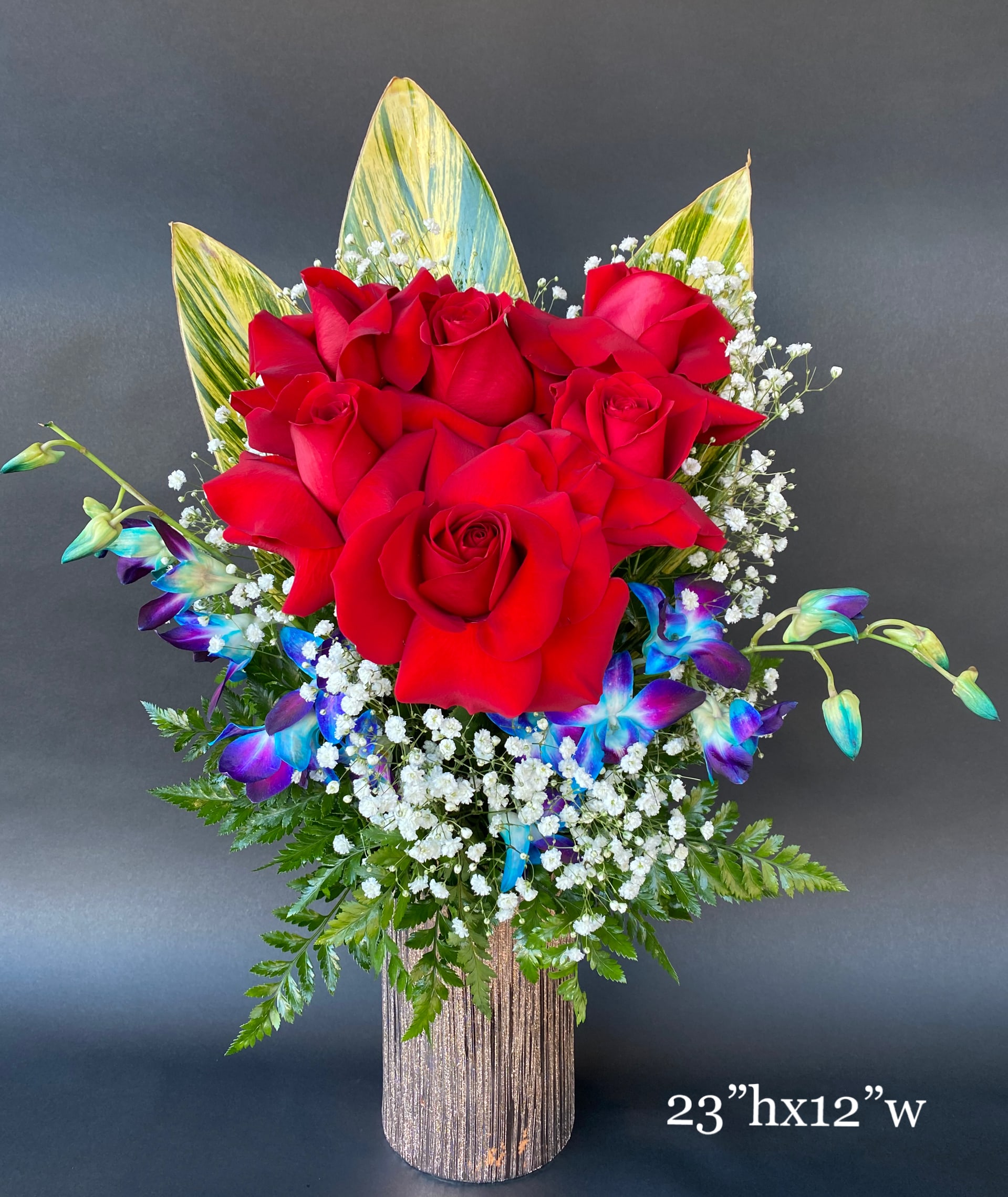 Red roses with blue orchids in a tall vase arrangement