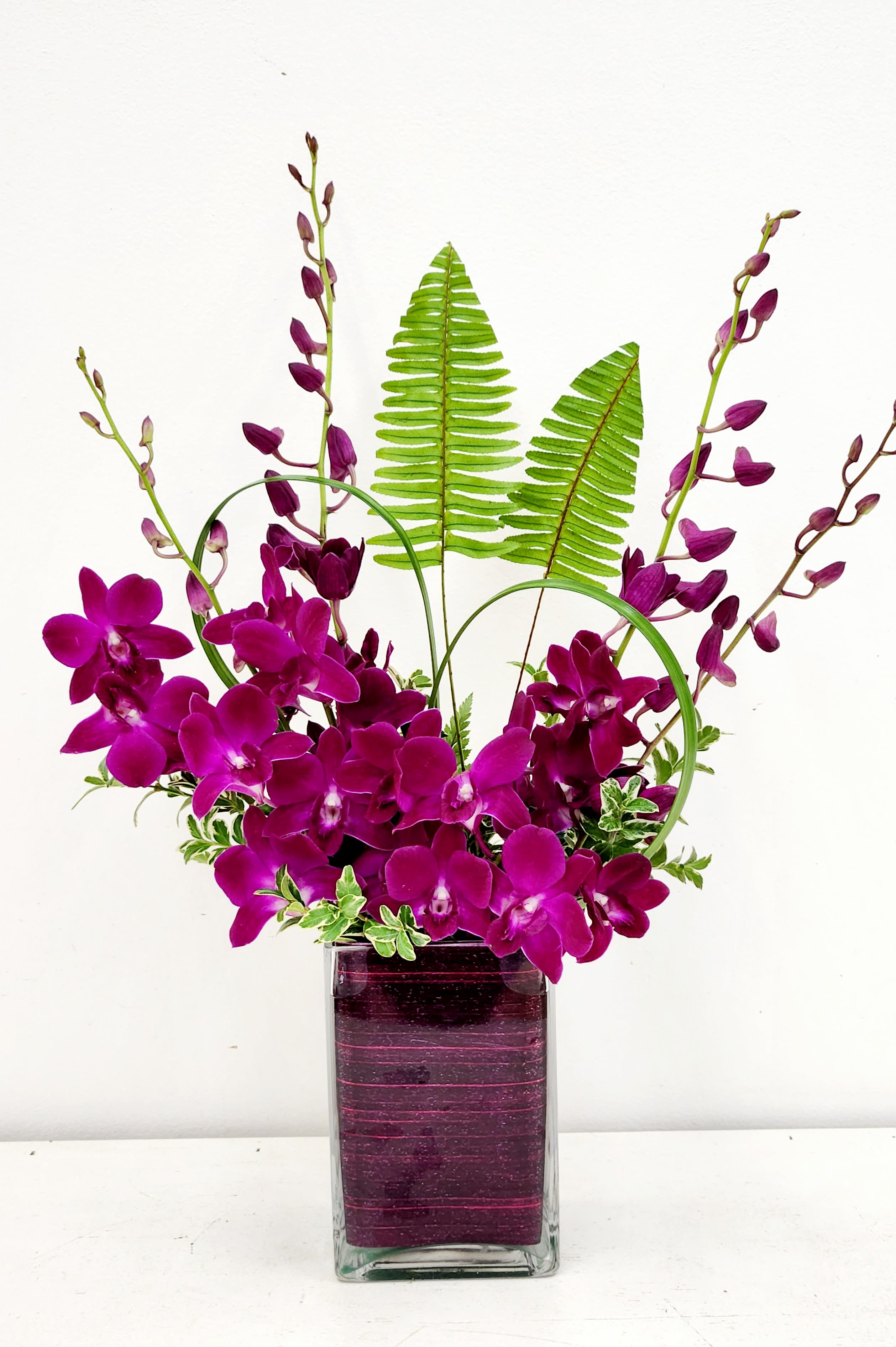 Orchid Symmetry - Vivid purple dendrobium orchids create an instant statement in this modern orchid arrangement-perfect as a birthday bouquet, a congratulations gift, or a romantic surprise. The design's strong vertical rhythm and jewel-toned color story make the recipient feel noticed and celebrated, whether placed on a dining table, desk, or entry console.  