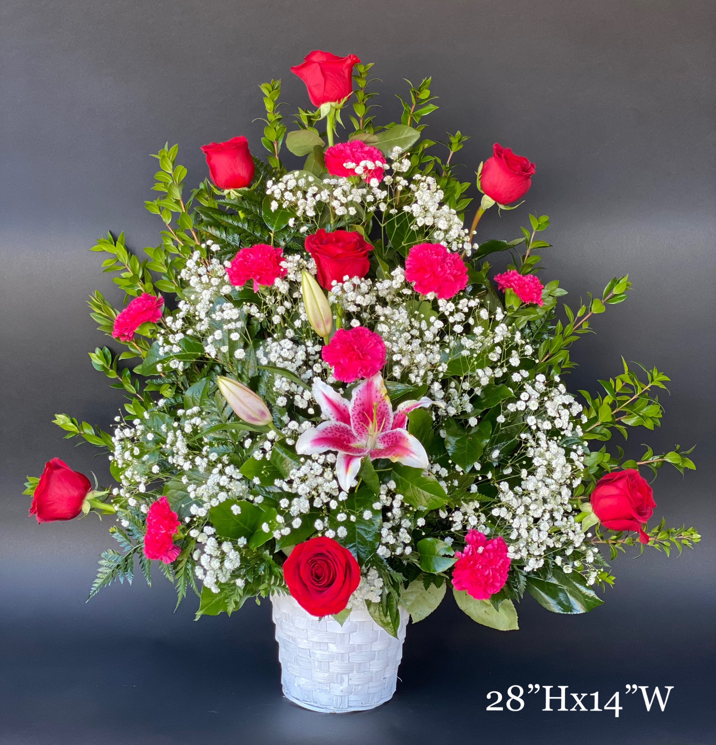 Tall bouquet of red roses, pink carnations, and a pink lily in a white basket vase