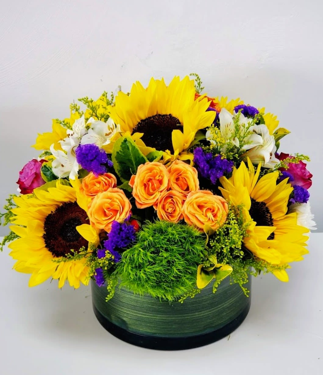 Sunshine  - Bright, sunny sunflowers take center stage in this cheerful flower arrangement, making it an ideal birthday bouquet, congratulations gift, or just-because surprise. The warm yellow-and-orange heart-large sunflowers encircling a cluster of orange roses-creates an immediate feeling of joy, while purple accent blooms and touches of white add contrast and depth that keeps the design lively and modern.  