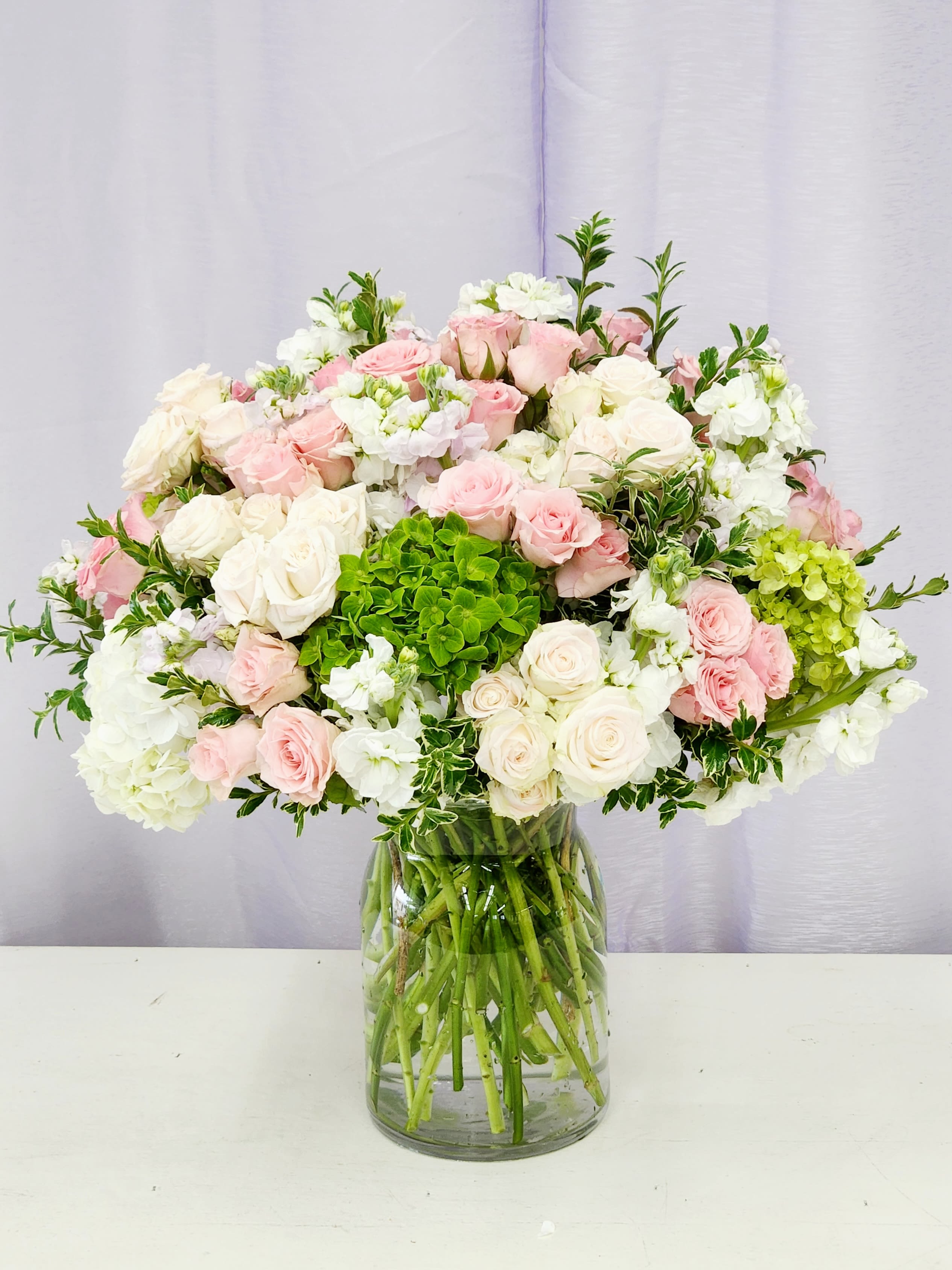 Touch of Elegance - A soft cloud of blush pink and white roses makes the flower arrangement a graceful choice for an anniversary bouquet, wedding table centerpiece, or a gentle celebratory gift. The first thing the recipient will notice is the lush, rounded shape and the fresh, airy feel that says "thoughtful" without being showy; it's the kind of gift that makes someone feel truly cherished.  \