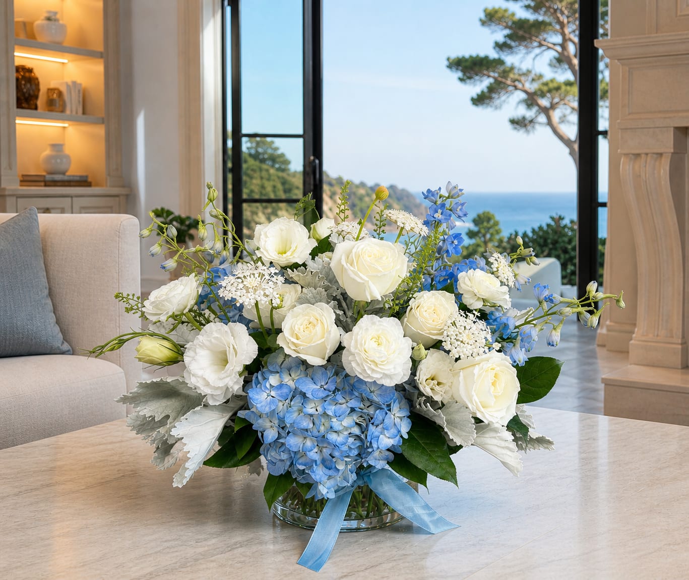 Coastal Elegance - Coastal Elegance brings together premium white roses, lisianthus, ranunculus, and airy textural accents, grounded by soft blue hydrangea and delphinium. Designed in a 6” x 6” glass cylinder, this arrangement captures the calm, polished feel of a Palos Verdes coastal home. Clean, balanced, and quietly luxurious—perfect for celebrations, gifting, or elevating everyday spaces.