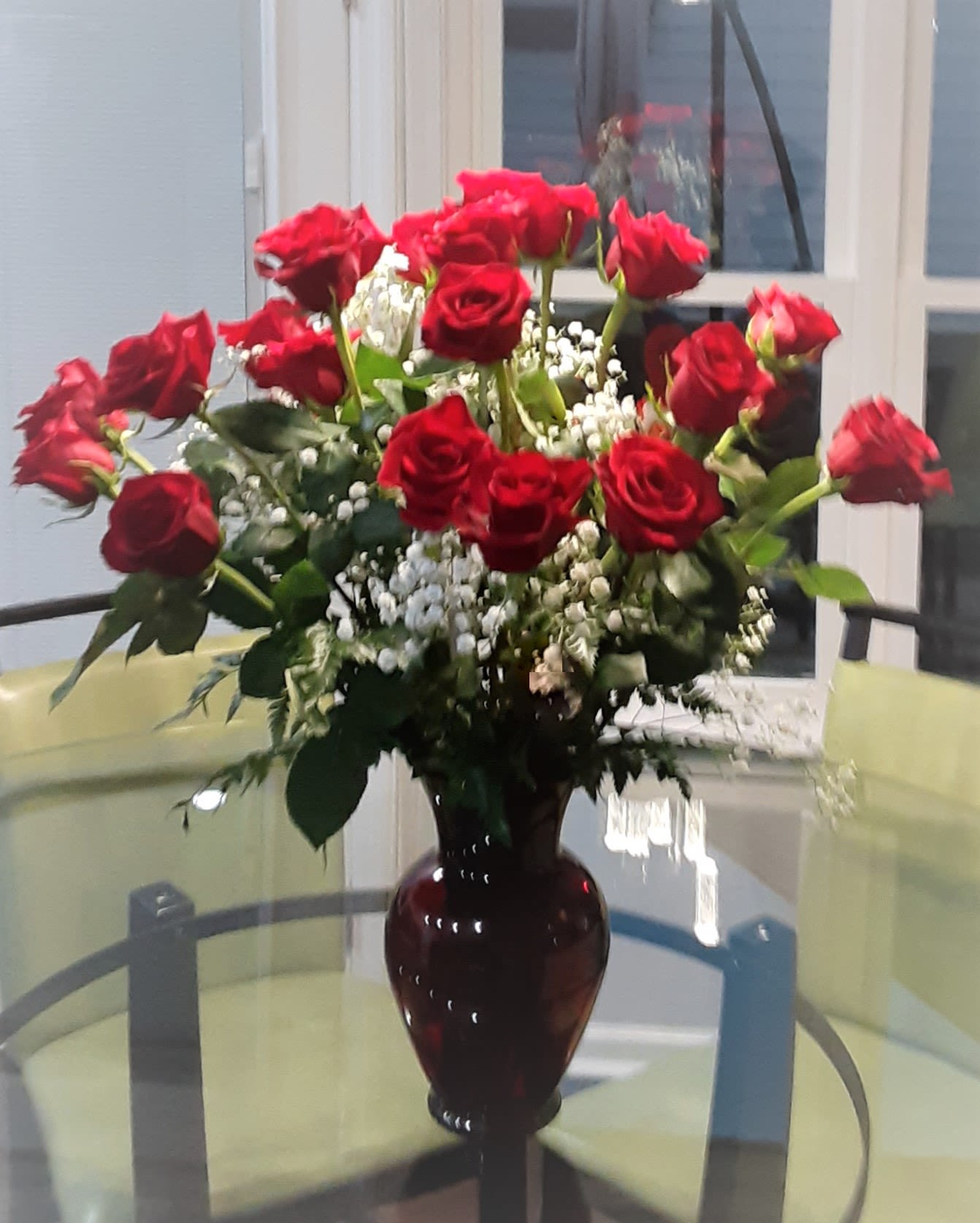 Red roses arranged in a dark glass vase with white filler flowers