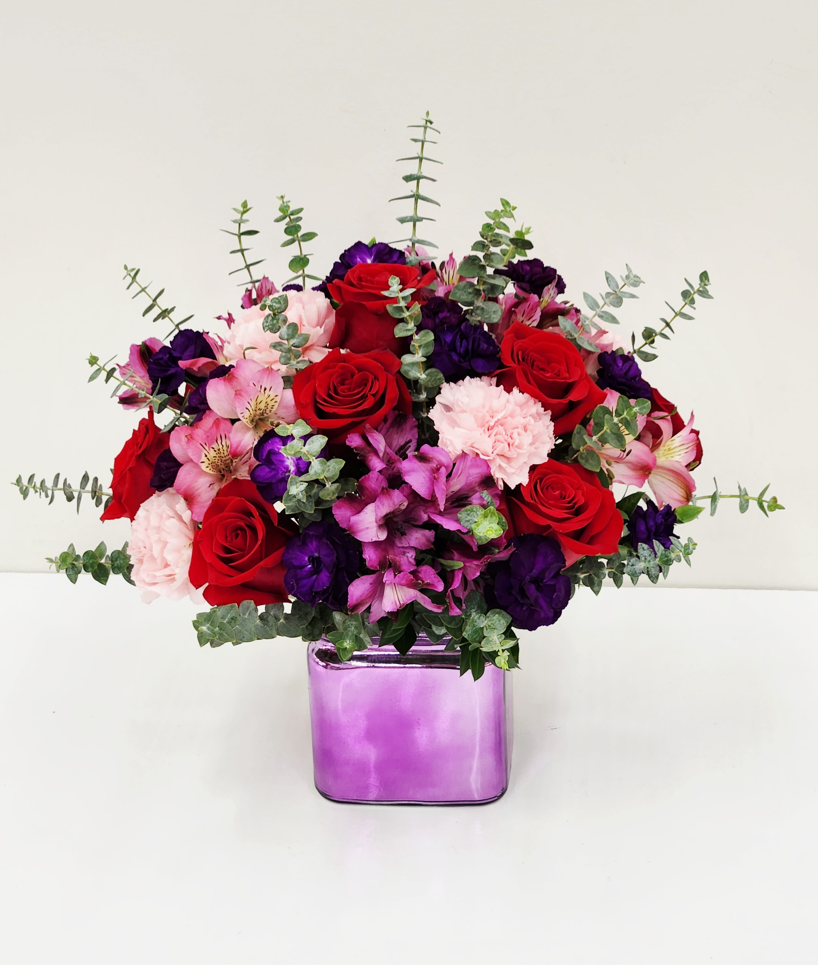 Playful - A lush combination of red roses, purple blooms, and pink alstroemeria and carnations creates an immediate feeling of warmth and celebration-perfect for a birthday bouquet, anniversary roses, or a spontaneous "thinking of you" gift. The arrangement reads romantic without being formal, so the person you're sending it to will feel both cherished and delighted by the vivid, joyful color story.  