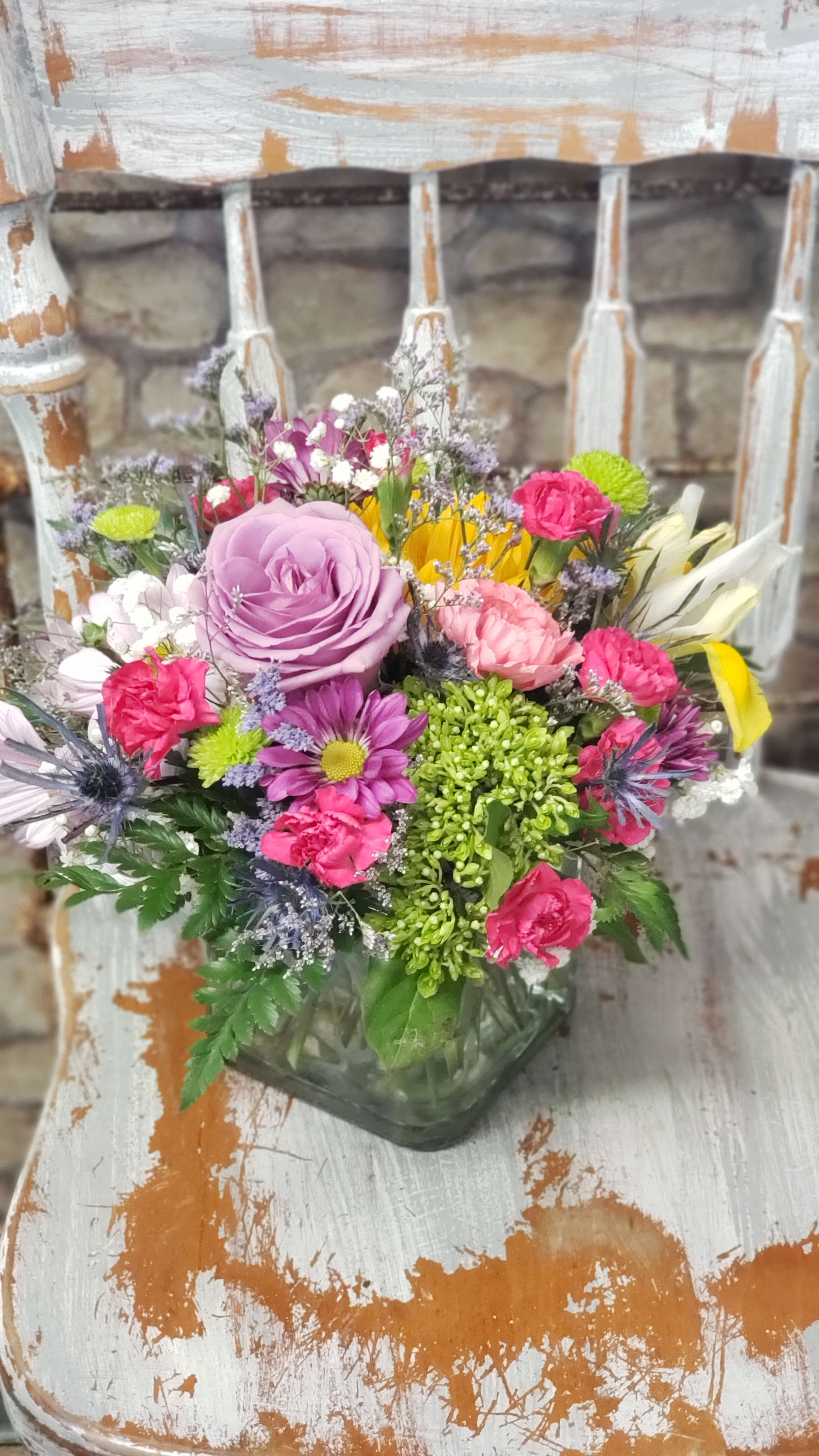 Colorful mixed flower arrangement with lavender rose, pink carnations, and daisies in a square glass vase