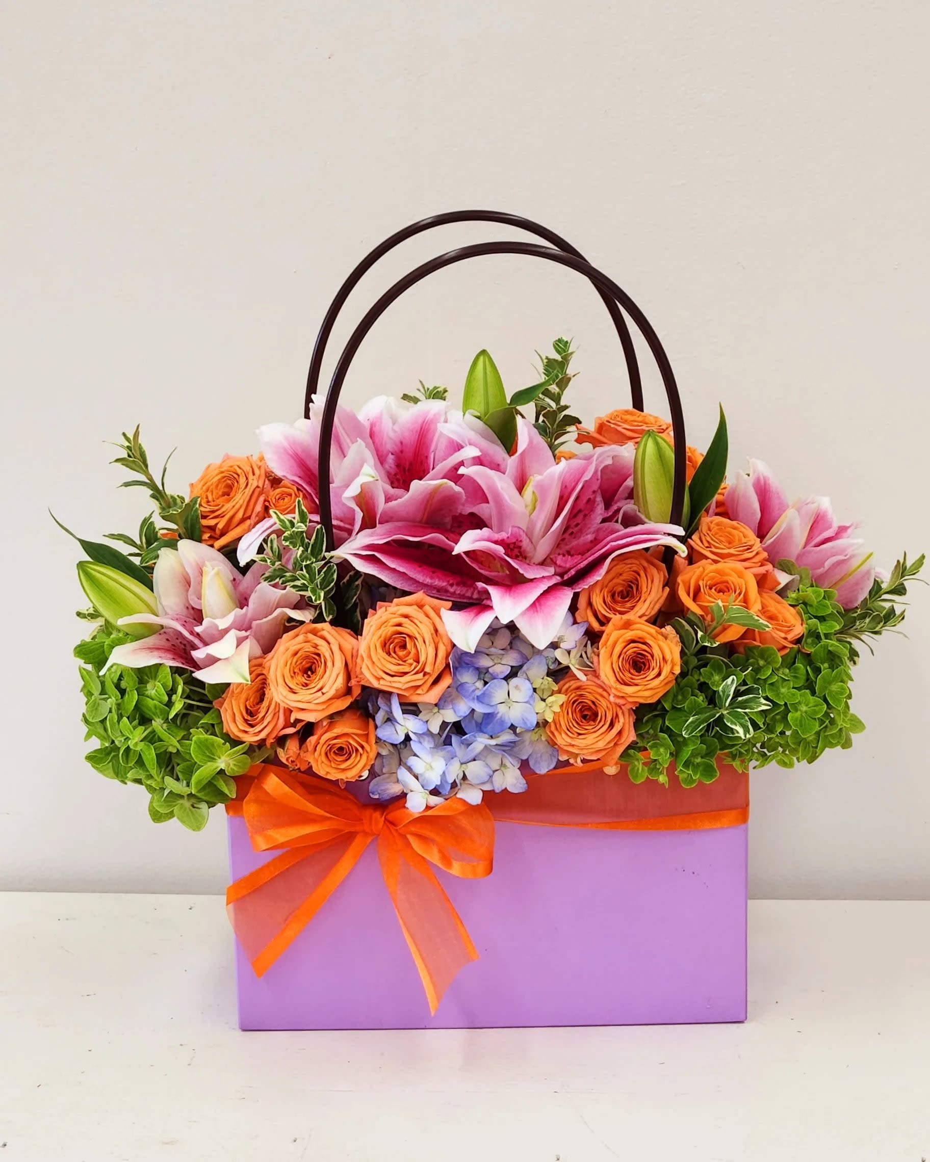 Roses and Lilies in a Bag - Big, fragrant pink lilies paired with clustered orange roses create an immediate, joyful impression in this compact flower arrangement-perfect as a Mother's Day gift, a Get Well pick-me-up, or a thoughtful Thinking of You surprise. The combination of warm orange and cool pink tones reads uplifting and celebratory, so the person you're sending it to will feel noticed and genuinely cheered the moment it arrives. Lift her spirit with this easy to carry bag of blooms.  