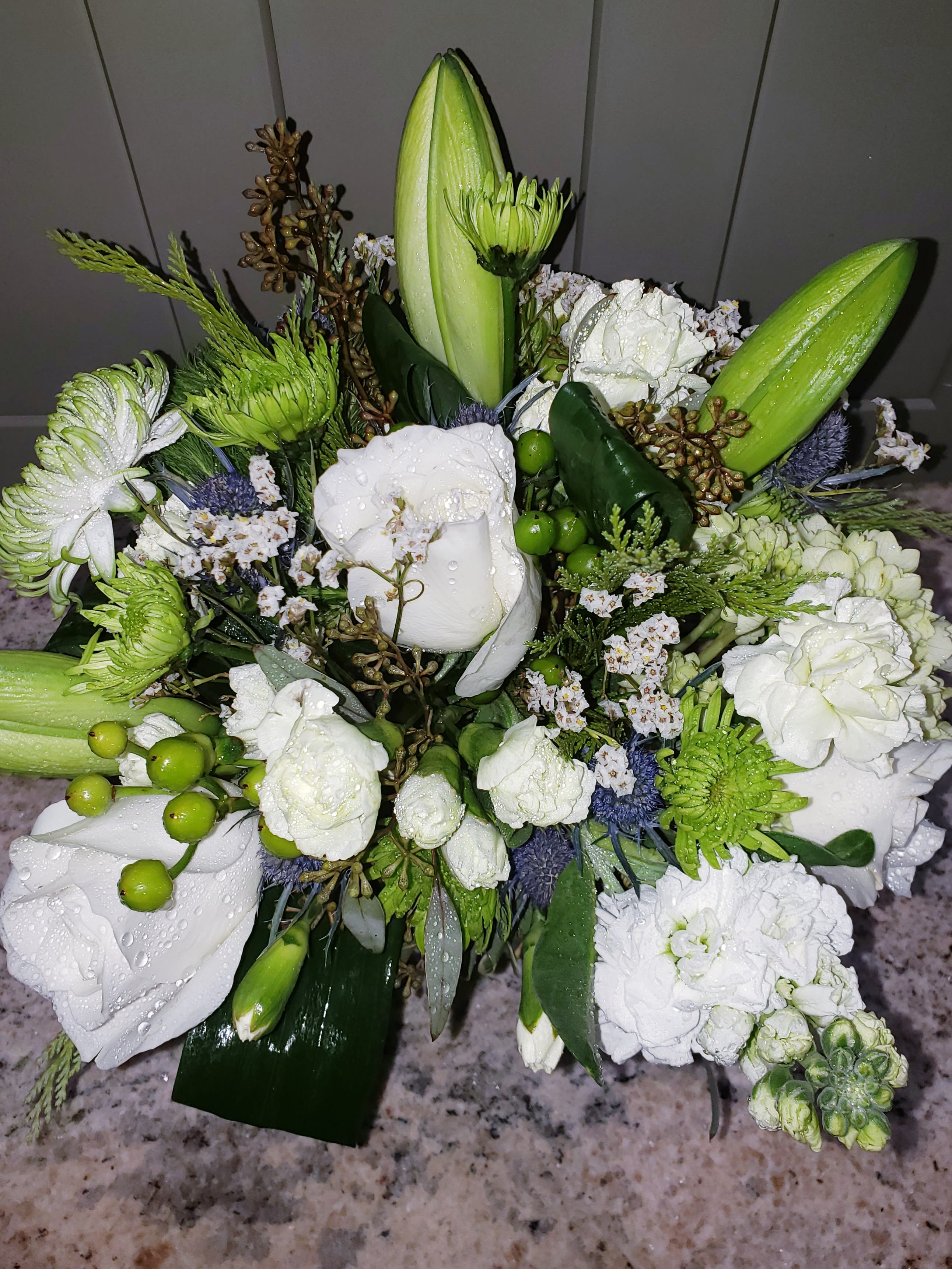 Compact arrangement of white roses, lilies, and carnations with green accents
