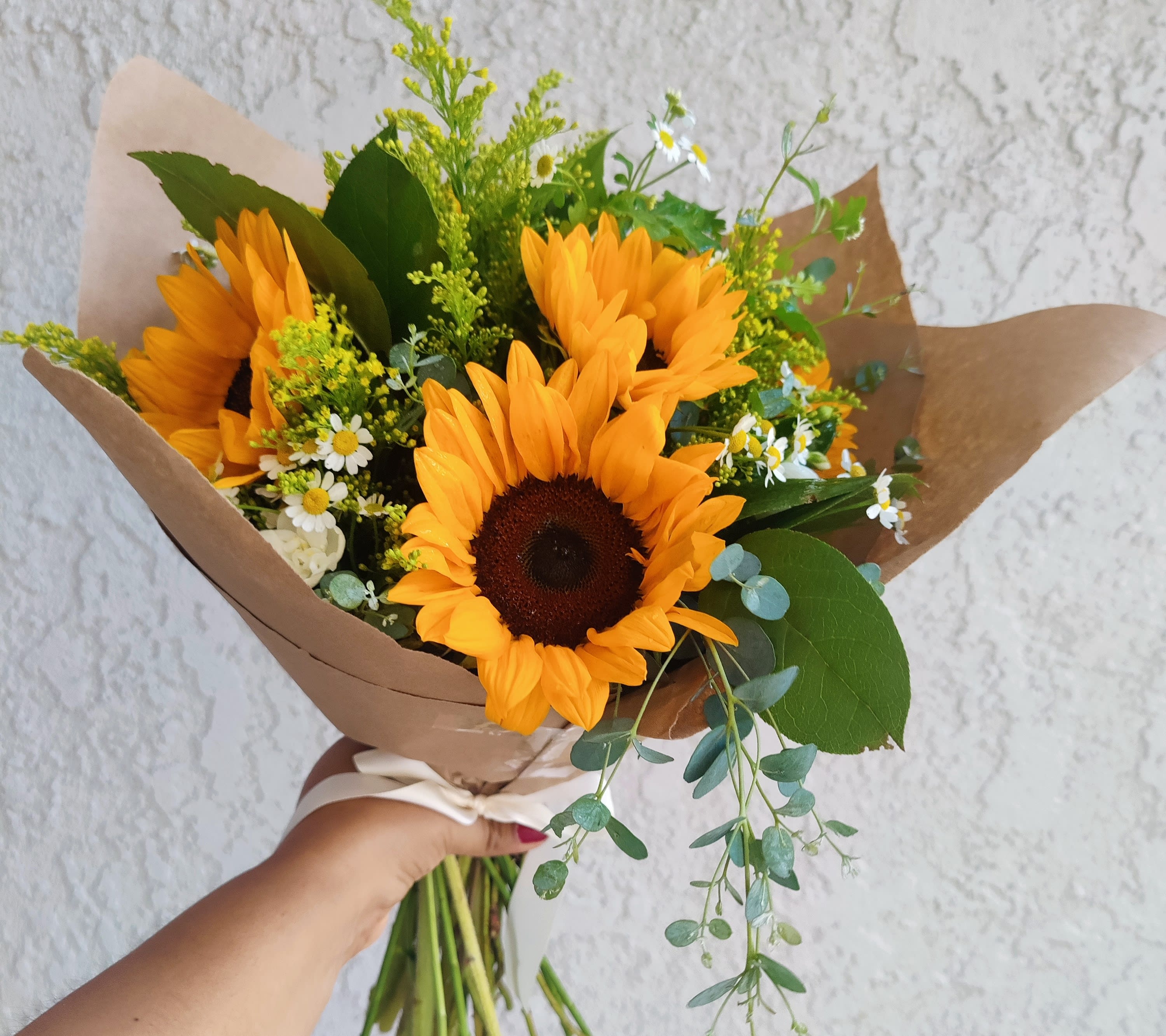 Handheld bouquet of sunflowers with small white daisies and brown paper wrap