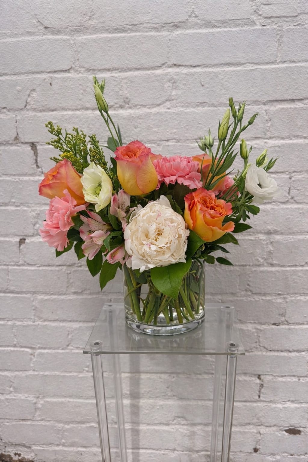 Mixed bouquet of pink, orange, and white flowers in a glass vase