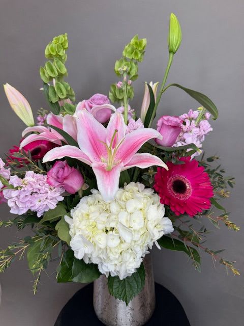 Pink lilies and mixed blooms arranged in a silver vase