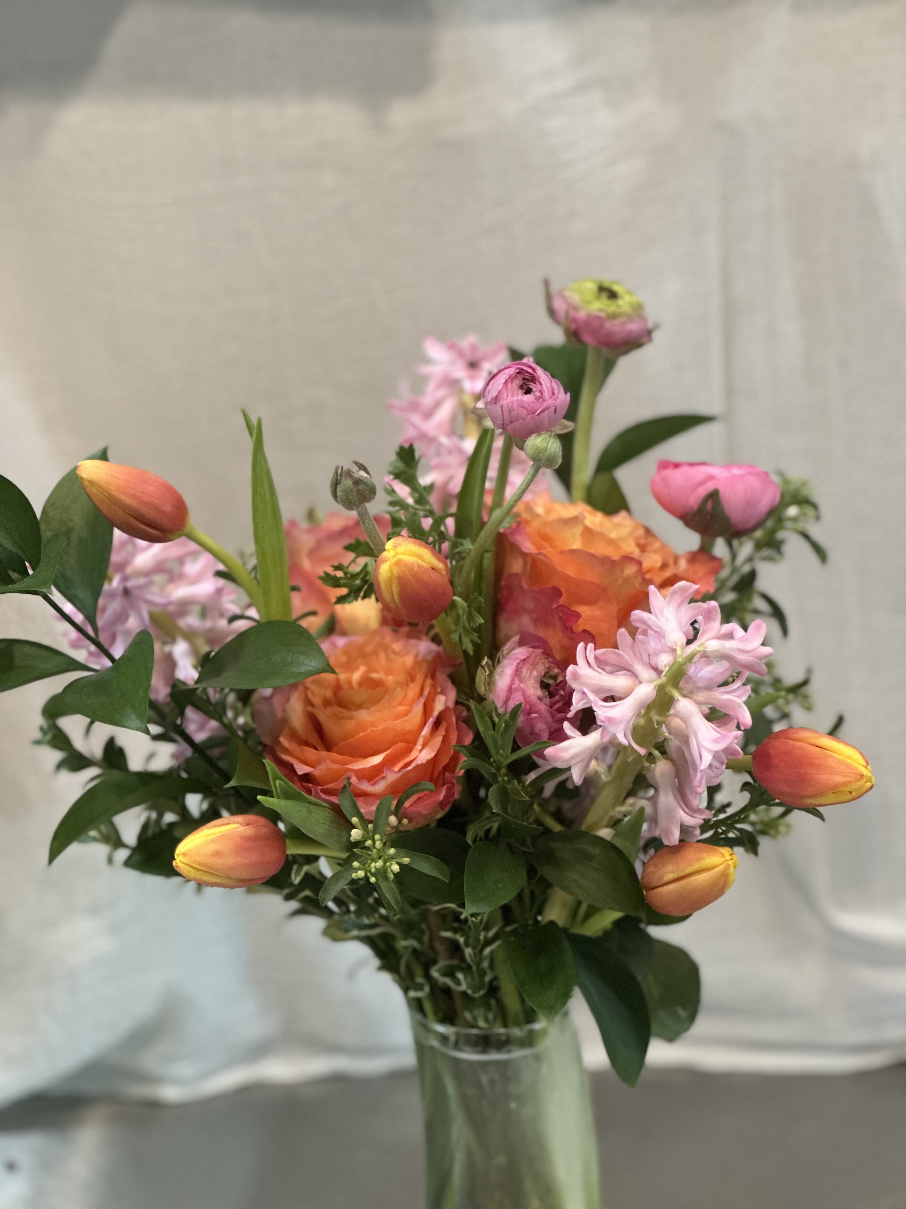 Mixed bouquet with orange roses, pink tulips, and pale pink blooms in a glass vase
