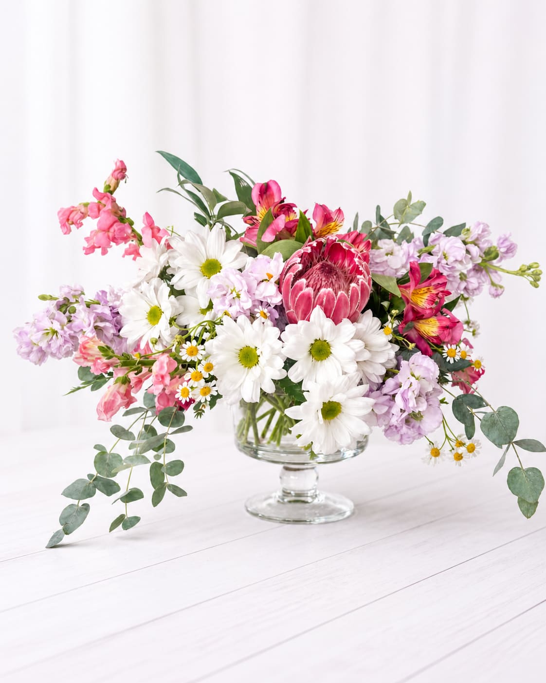 Mixed bouquet in a clear glass pedestal vase with pink, white, and lavender flowers
