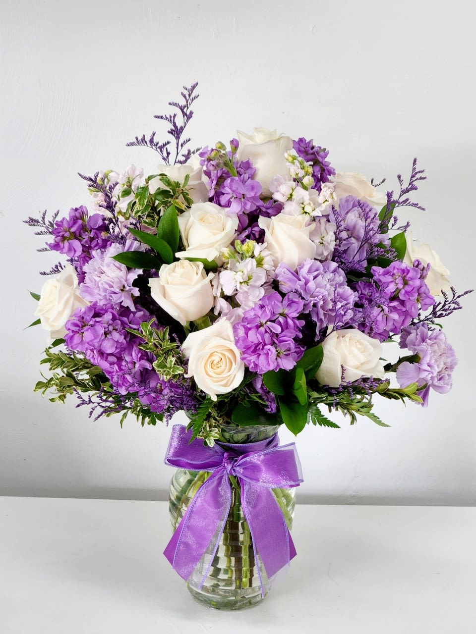 Angel's Grace - Soft white roses paired with clusters of vivid purple stock and light lavender carnations give this flower arrangement a romantic, spring-fresh presence perfect for most occasion. 