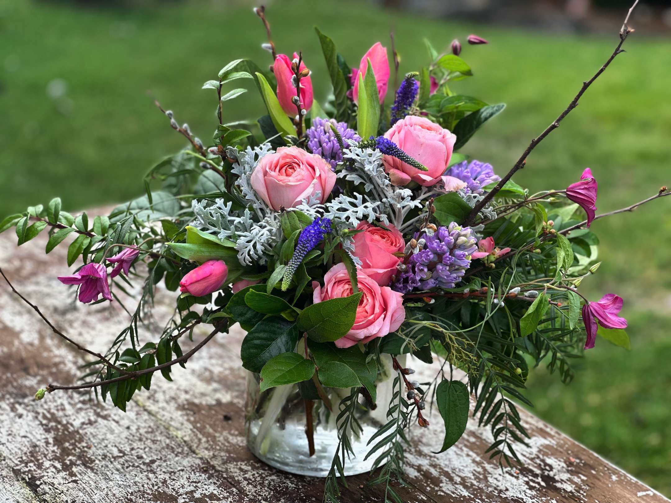 Pink roses and purple flowers in a clear glass vase with branches