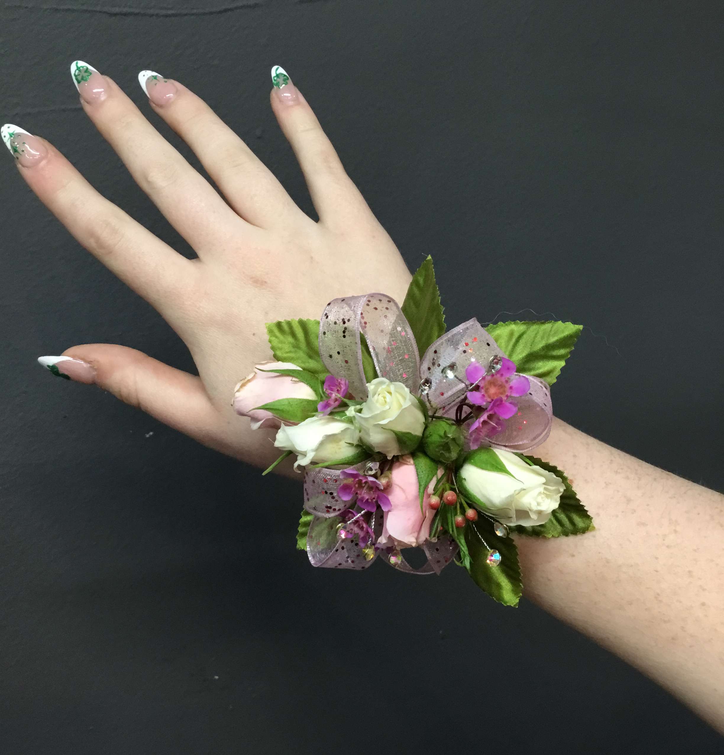 Wrist corsage with small white and pink roses and purple accents on a person’s arm