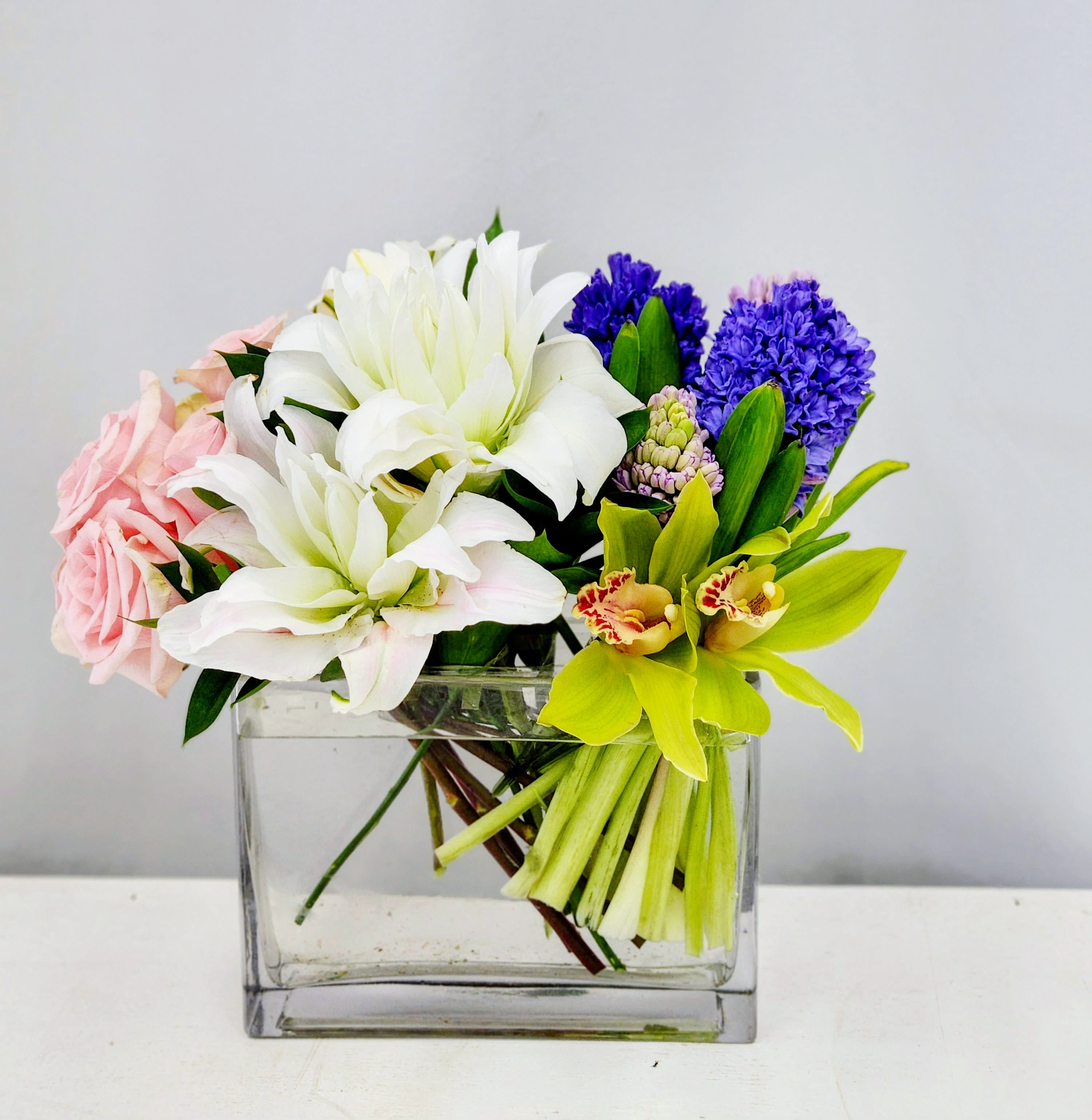 Uniquely You - Compact clear rectangular vase of white lilies, pink roses, purple hyacinth and yellow-green orchids - expertly designed uniquely just for her.