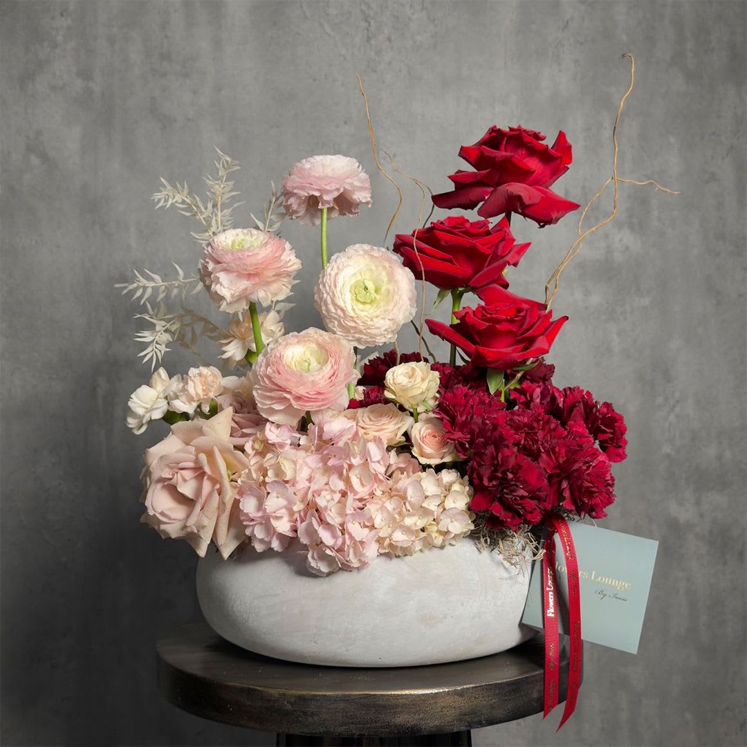     Scarlet Blush Atelier - An artistic arrangement blending soft blush florals with rich crimson accents, featuring roses, ranunculus, hydrangea, and textured elements in a modern ceramic vase. Elegant, sculptural, and expressive, this design creates a refined statement for special occasions or elevated interiors. Custom greeting card included.