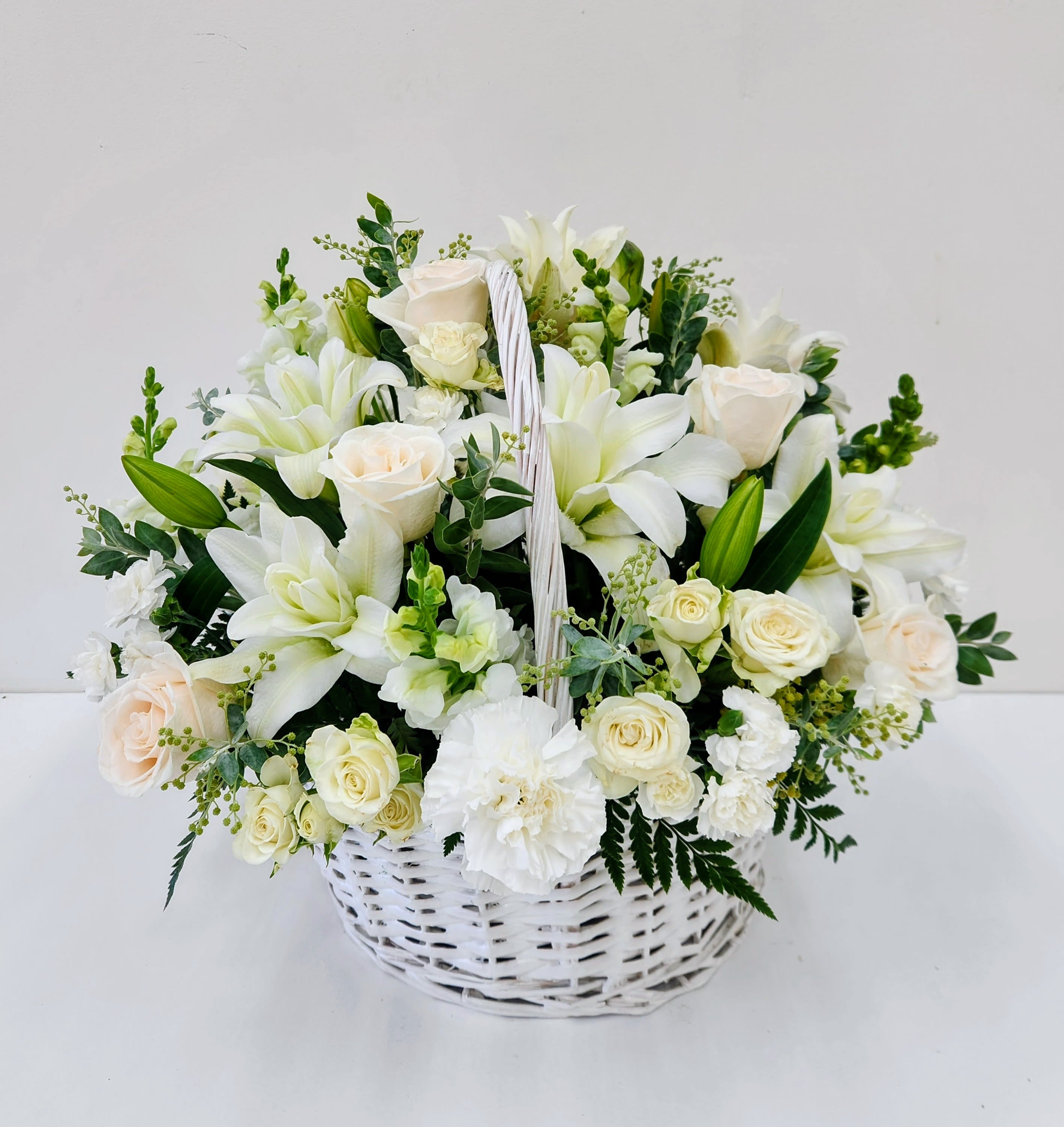 White Basket of Blooms - White wicker basket overflowing with white lilies, roses, carnations and snapdragons with soft green accents.