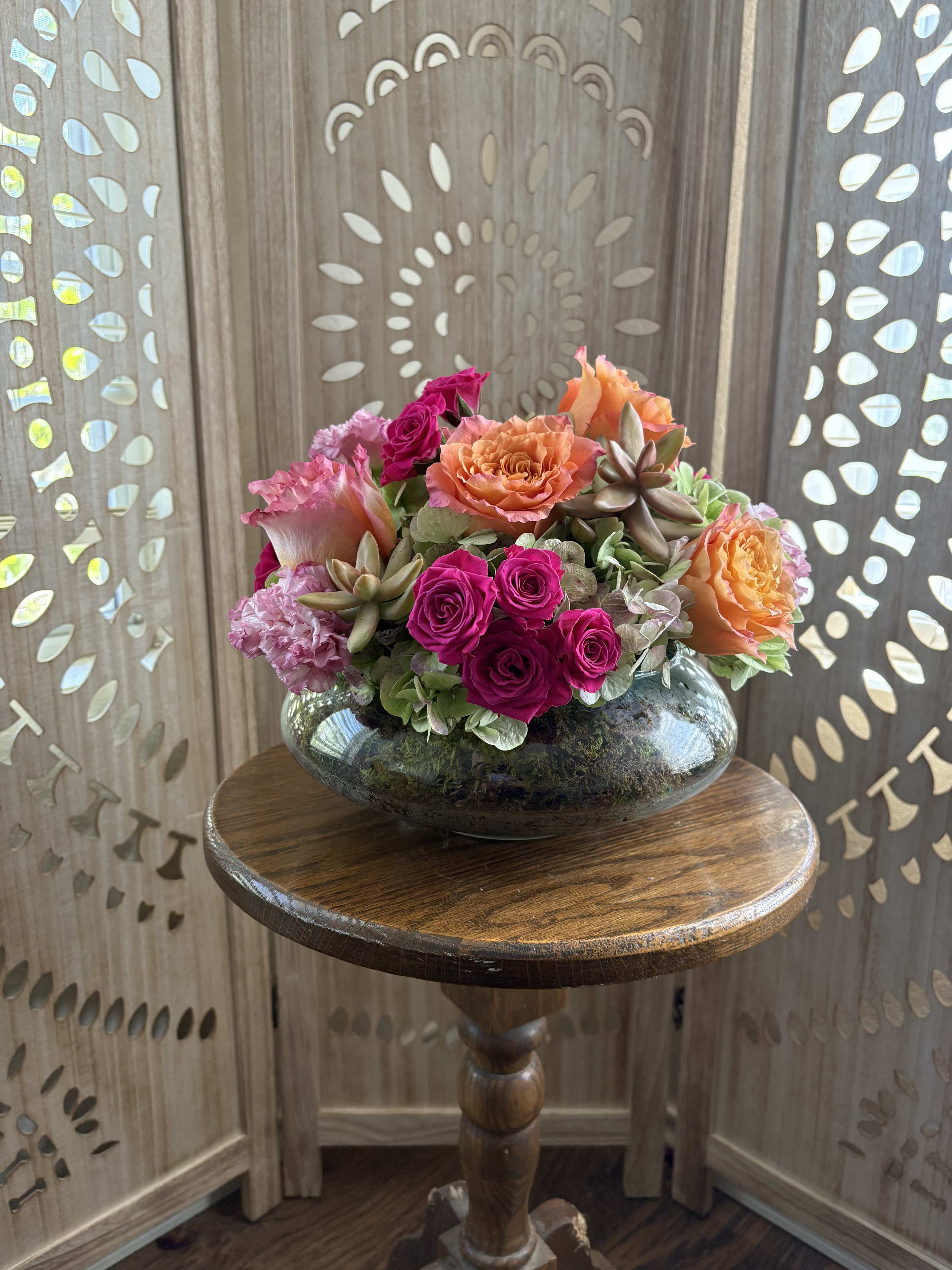 Bloom Babe - A vibrant mix of orange Free Spirit roses, hot pink spray roses, hydrangea, and blush lisianthus layered with sculptural succulents and tucked into a bed of natural sheet moss. This design brings bold color and soft garden texture together in a way that feels both playful and grounded