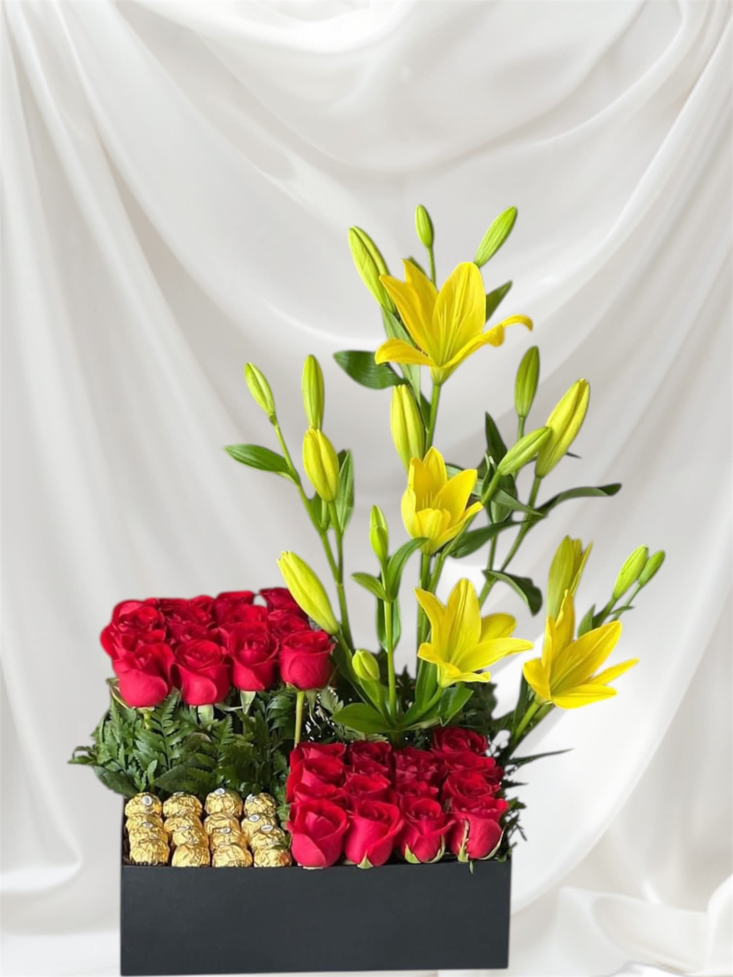 Red roses and yellow lilies arranged in a black box with chocolates