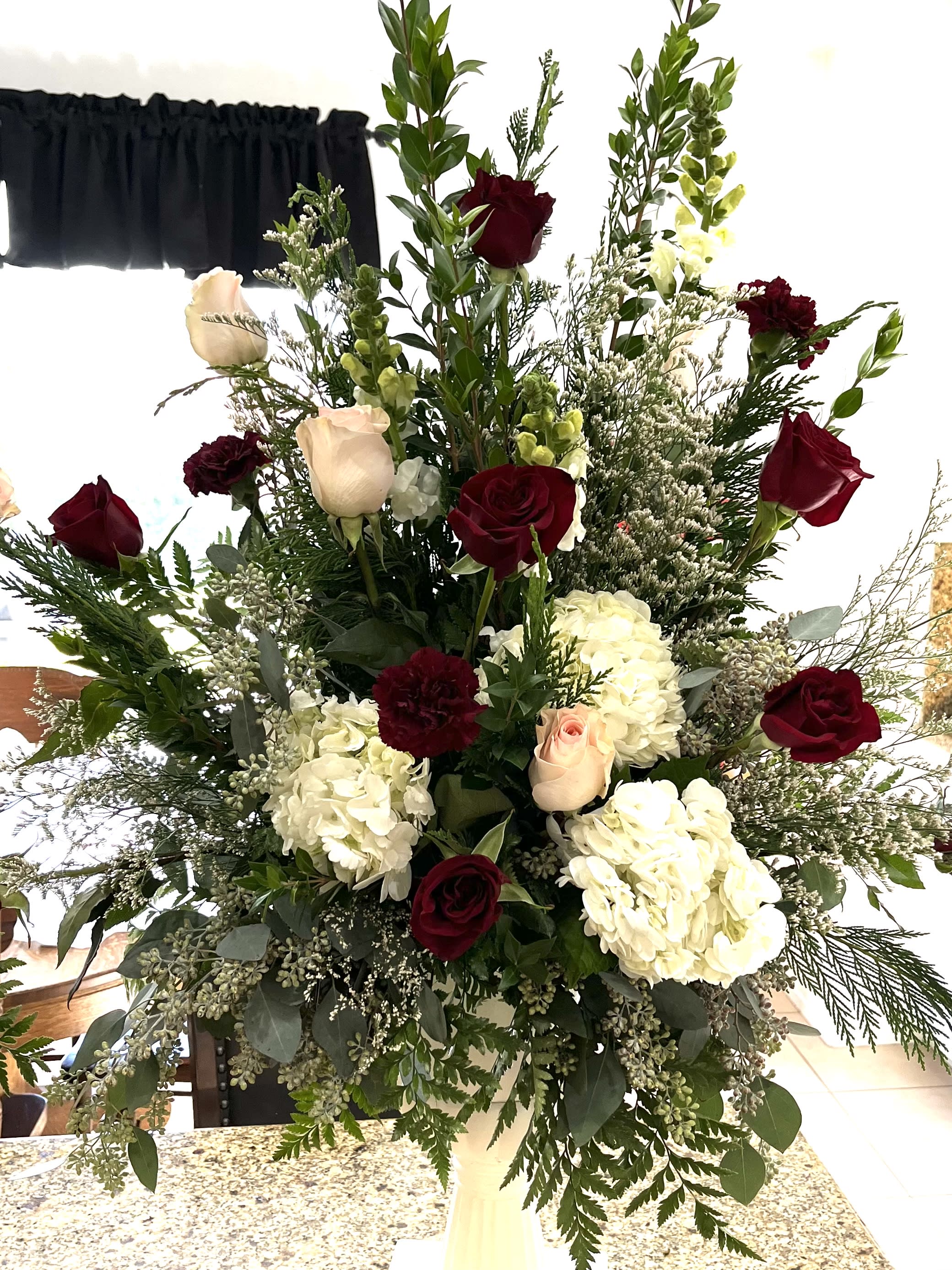 Tall arrangement of red and blush roses with white hydrangeas in a vase