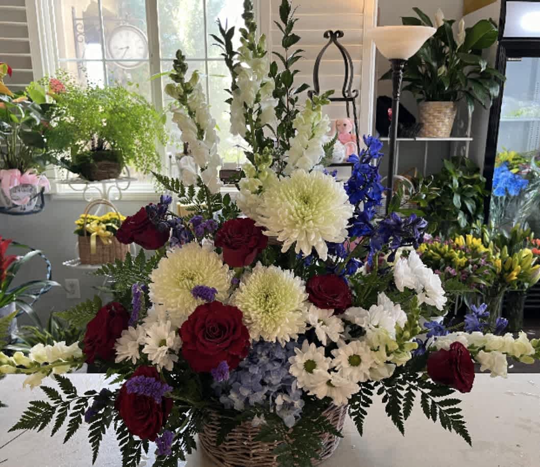 Large mixed flower arrangement in a wicker basket with red roses and white blooms