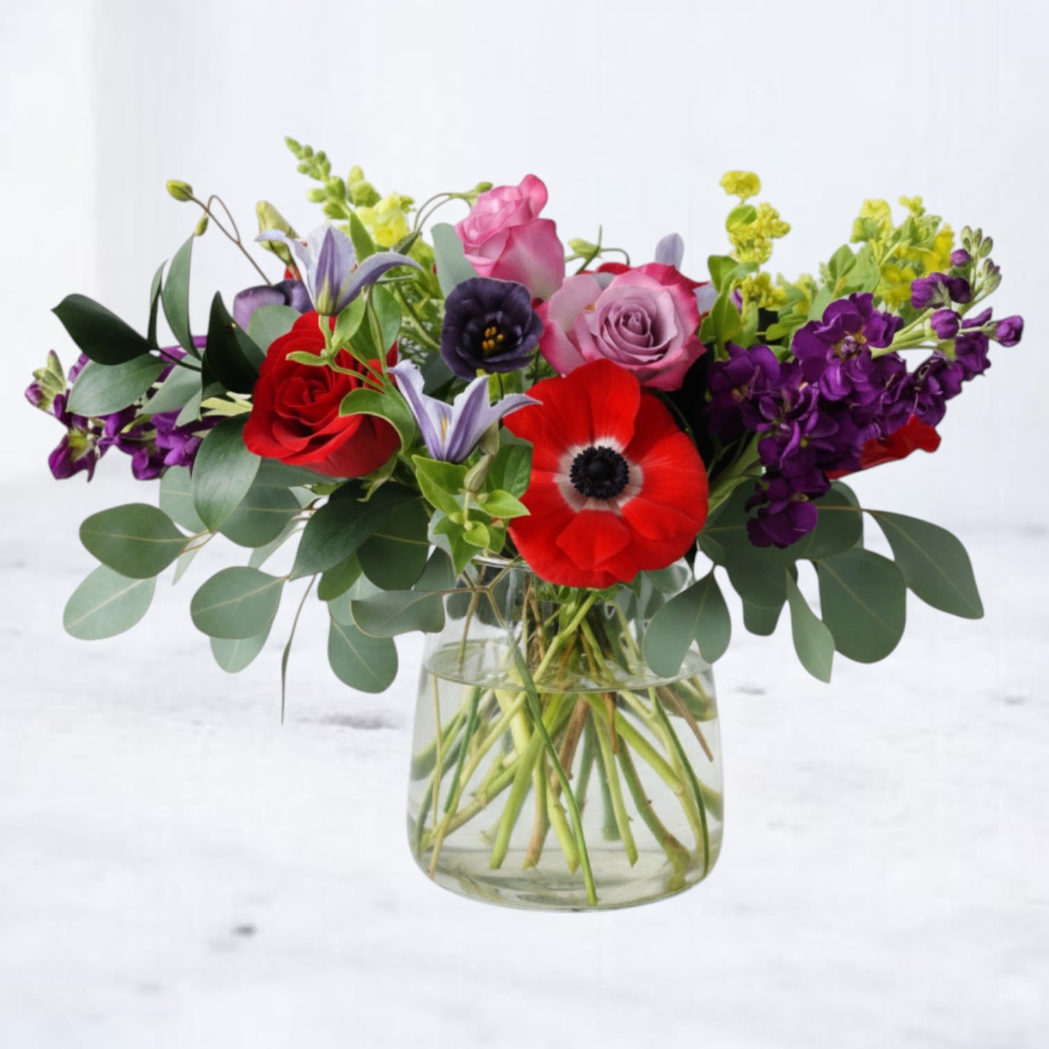 Mixed bouquet of red, pink, purple, and yellow flowers in a clear glass vase