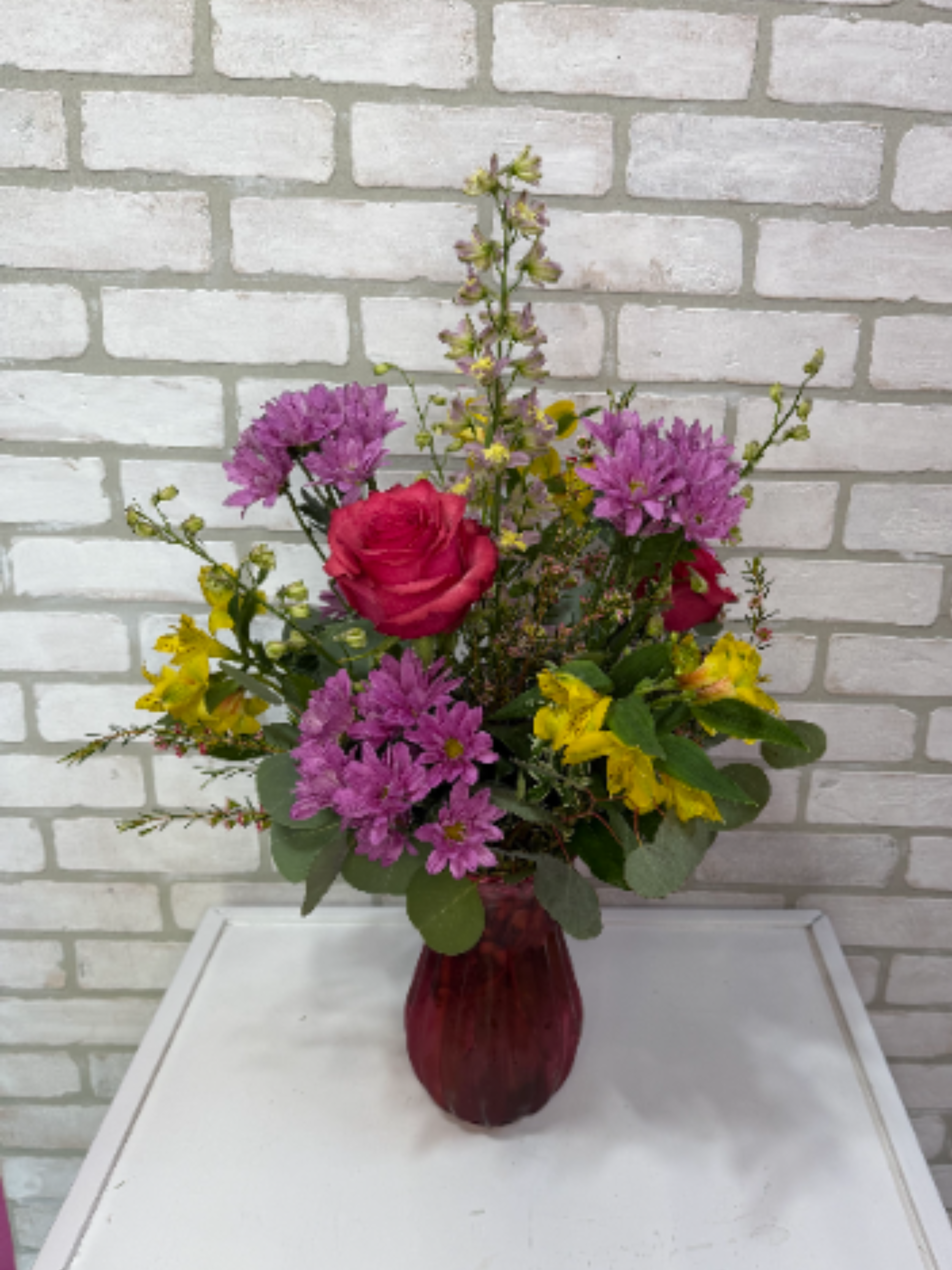 Garden of Love - A colored vase arranged with daisies, alstroemeria lilies, larkspur, and roses. 