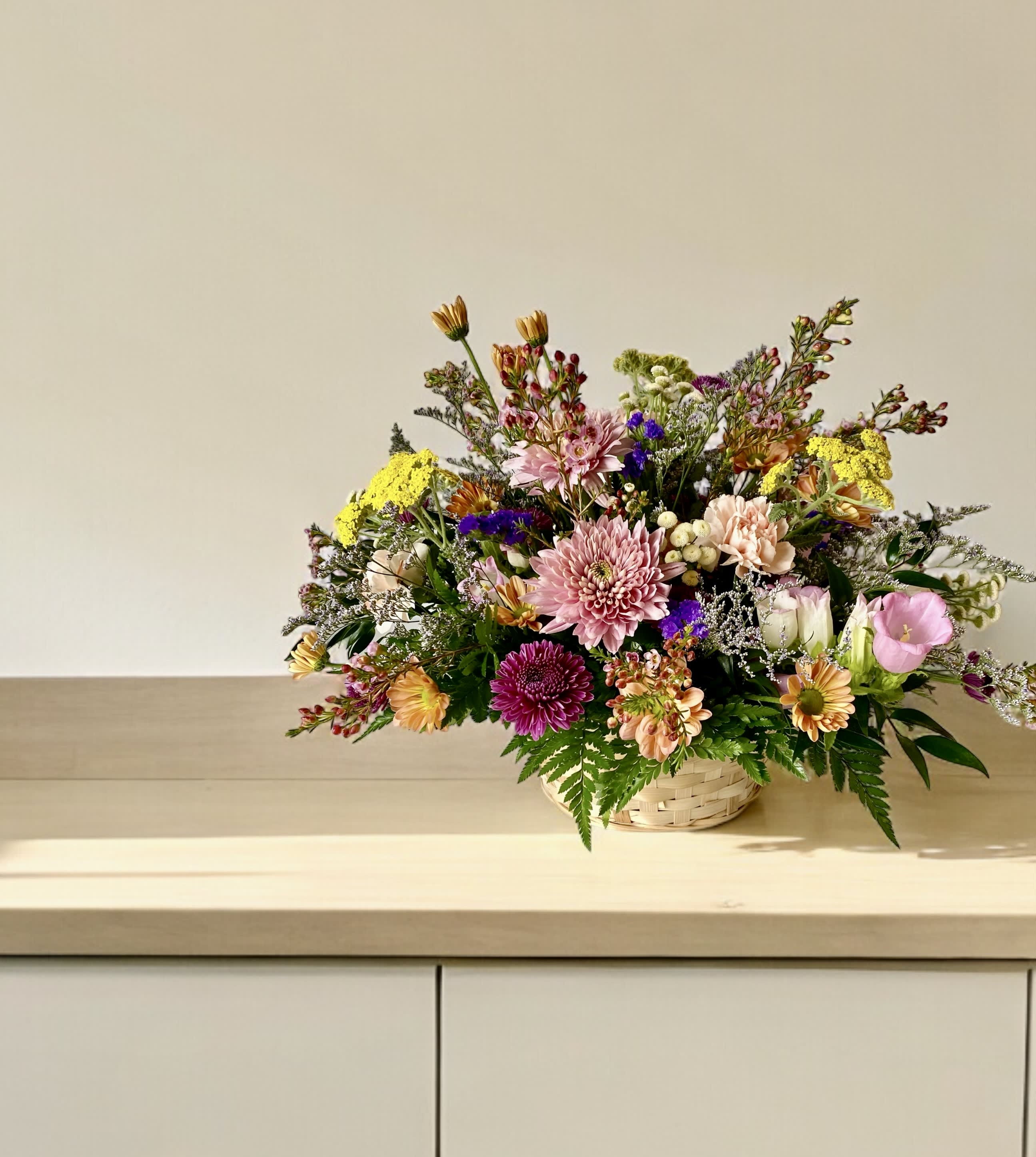 Mixed bouquet in a woven basket with pink, yellow, and purple flowers