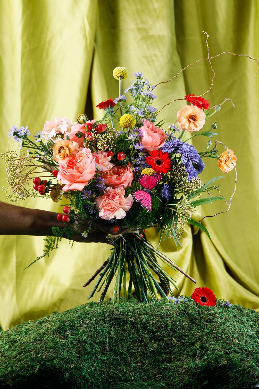 Ladies of Garden - Ms. Ladybug  - Bold, vibrant, and full of life, Miss Ladybug brings a playful energy to the garden. Designed in rich reds, corals, and warm seasonal tones, this arrangement features a lively mix of blooms that feel both joyful.  Layered with textural greenery and clustered florals like Dragonfly rose, Micro Gerbera, lavender aster, and other interesting blooms that make this composition feel intentional and full, like a garden carefully watched over. Each element is placed with purpose, creating a wild and free bouquet.  Hand-tied and ready to display, this piece honors the mother who protects, prepares, and shows up—again and again—with love that is both fierce and tender.  To keep your blooms fresh, trim stems and refresh water every two days.  Please note that this bouquet is exclusive to Mother's Day, May 8th-10th.