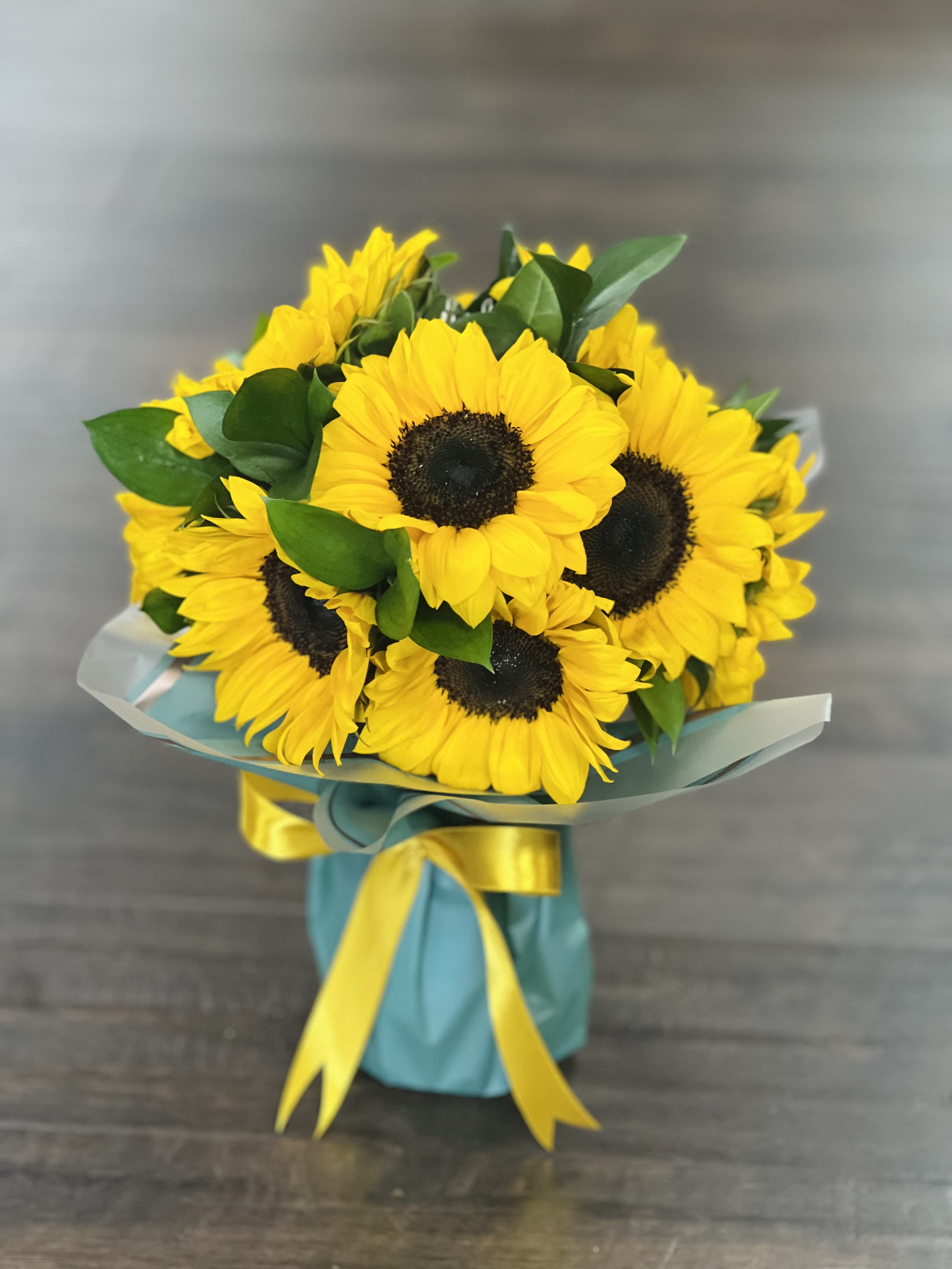 Bouquet of yellow sunflowers wrapped with blue paper and ribbon