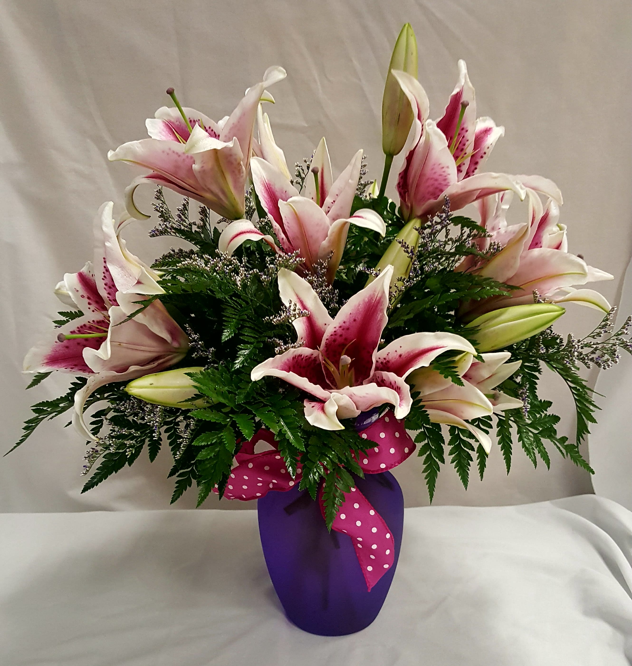 Pink and white lilies arranged in a purple vase with a polka-dot ribbon