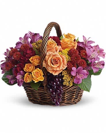 Basket of peach roses and purple flowers with grapes