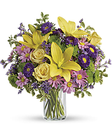 Yellow lilies and purple daisies in a clear glass vase