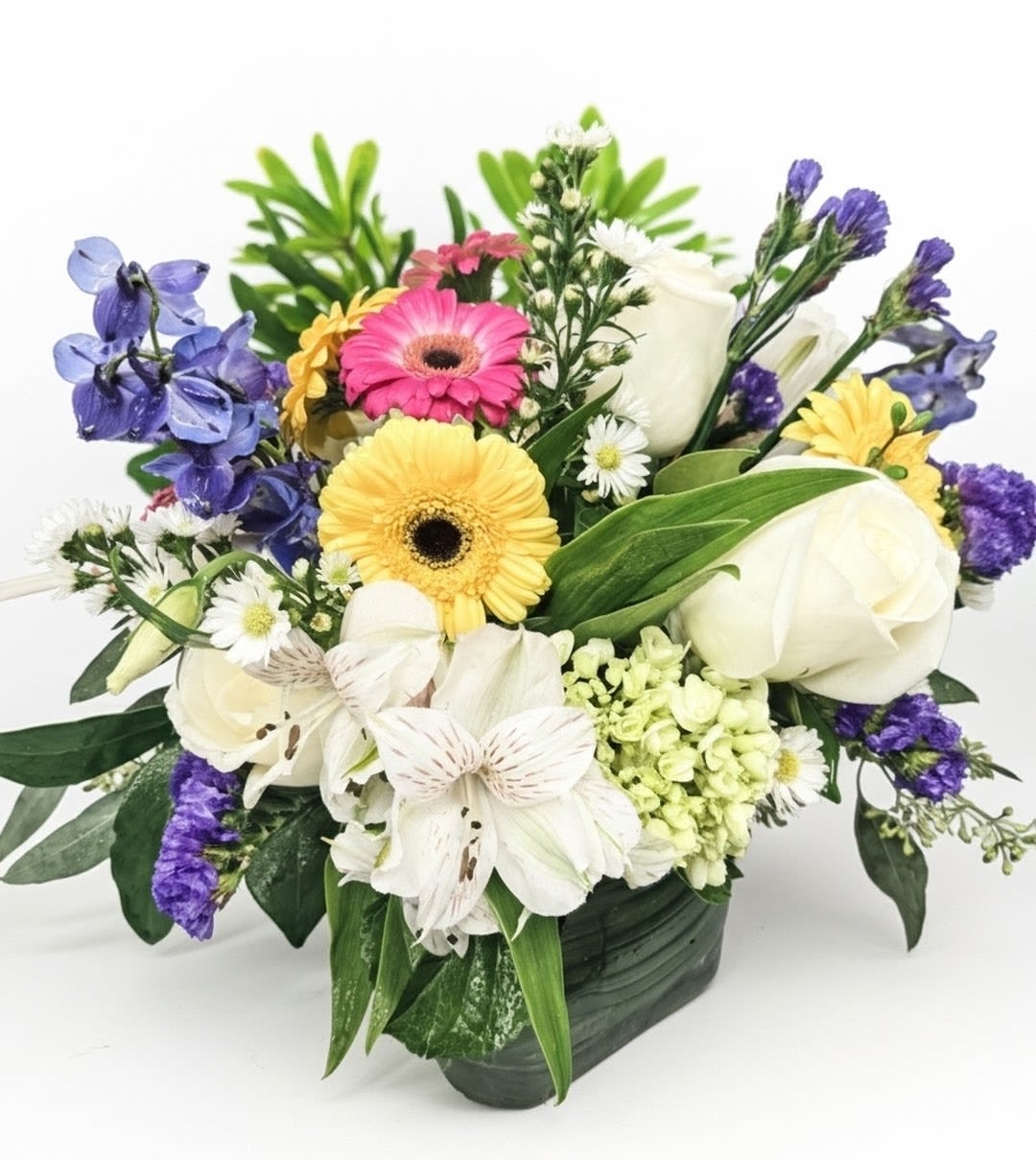 Colorful mixed flower arrangement with gerbera daisies and white roses in a square glass vase