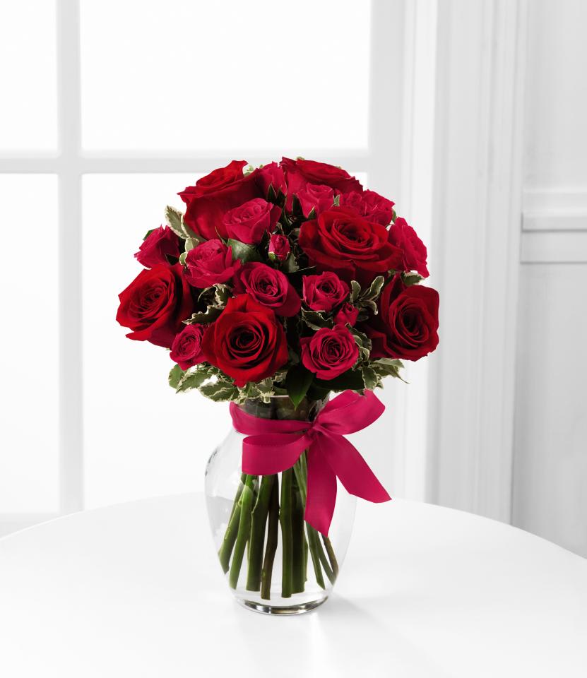 Red roses arranged in a clear glass vase with a pink ribbon