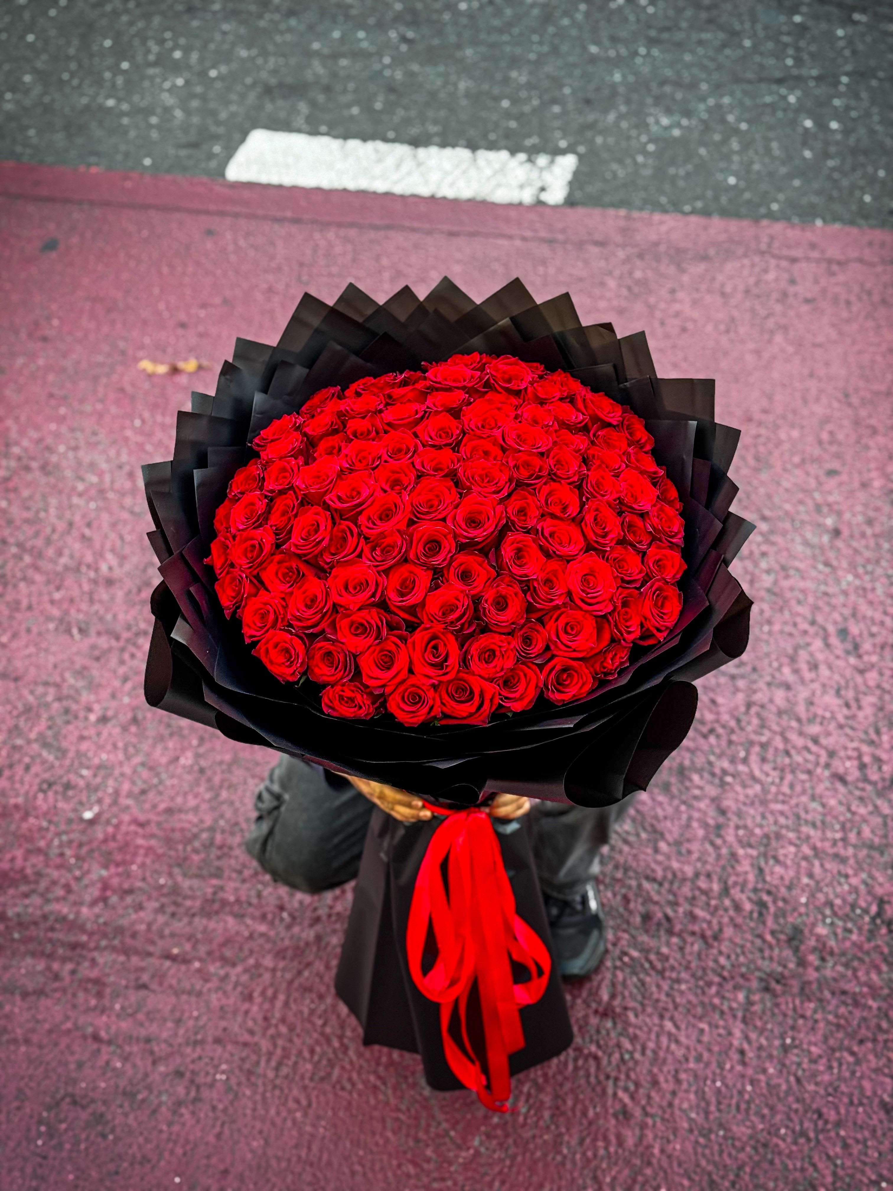 Royal Red Dome- 100 Rose Bouquet - The ultimate symbol of love and luxury. This full dome arrangement of premium red roses is crafted to perfection, wrapped in sleek black paper for a bold, timeless finish. Designed to impress at first glance.