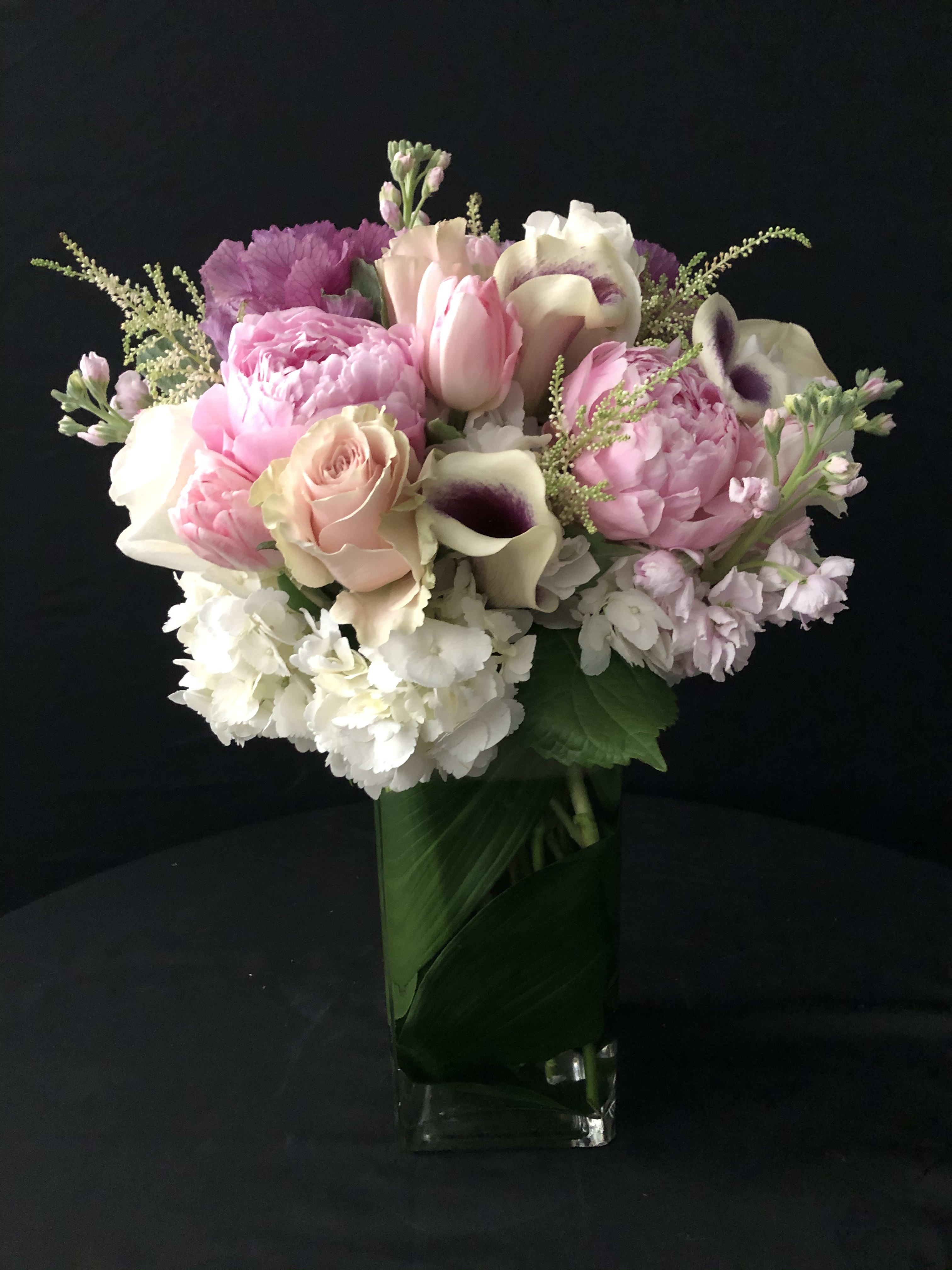 Tall arrangement of pink and white flowers in a clear glass vase lined with green leaves.