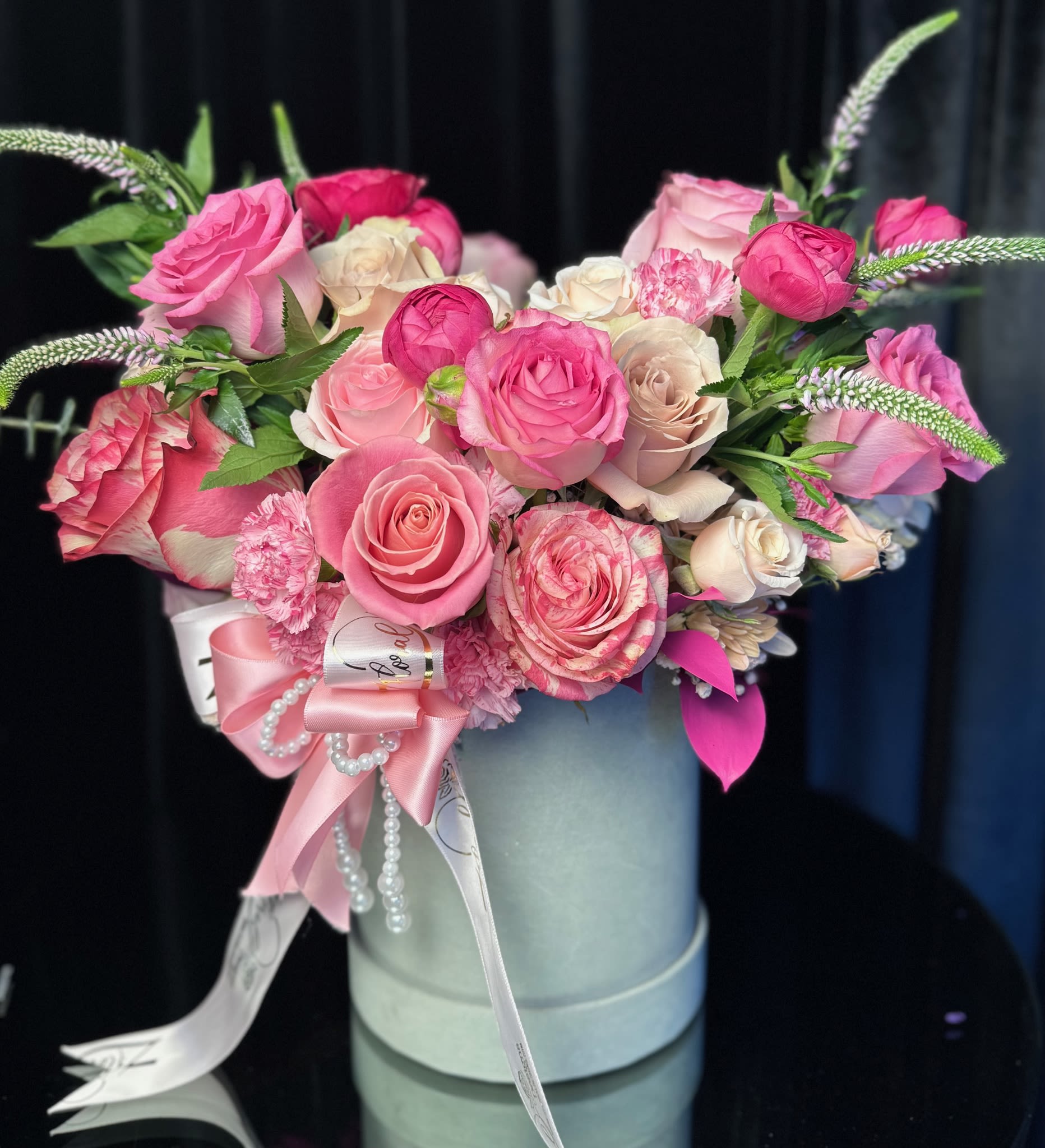 Pink and white roses arranged in a round hatbox with ribbon and pearl accents