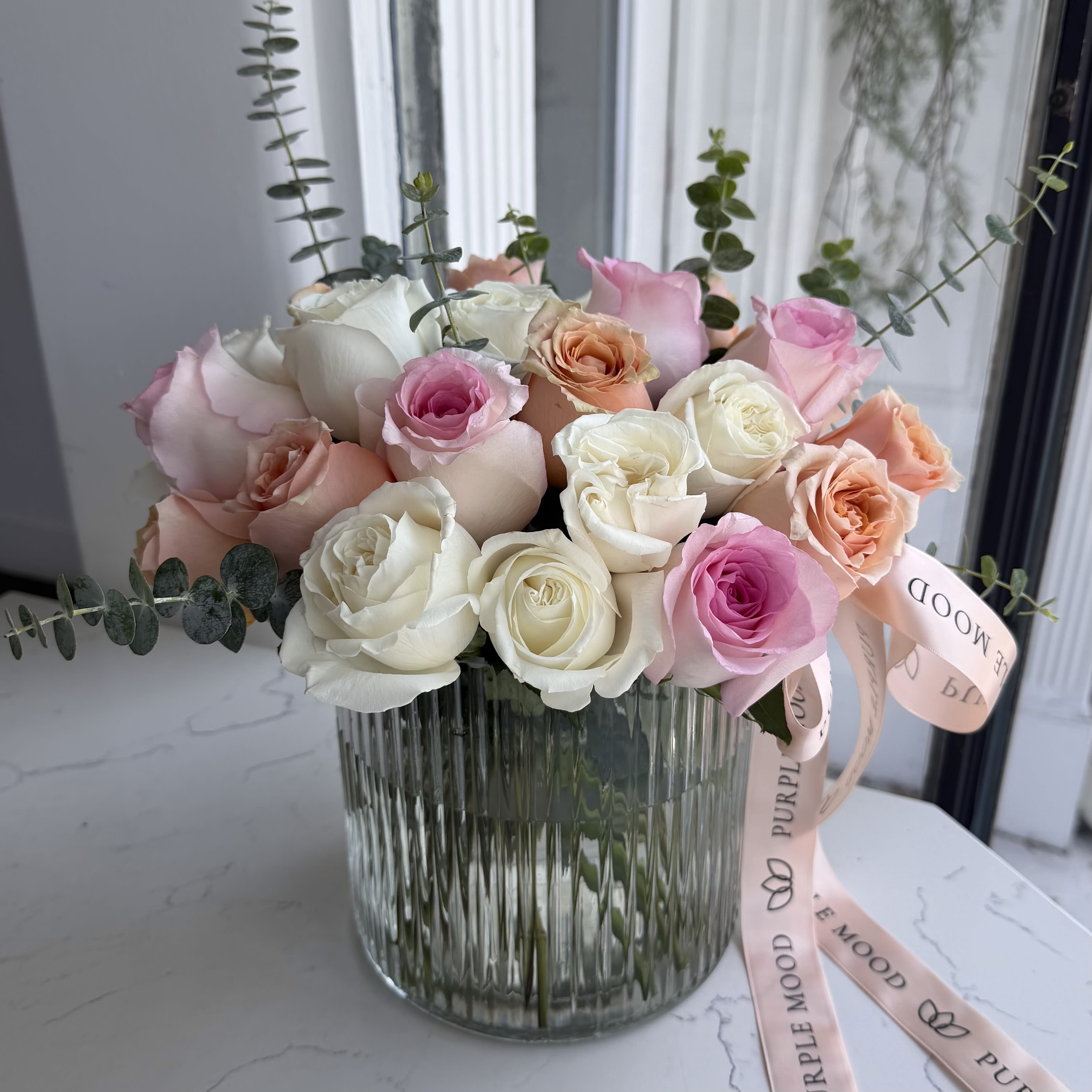 Blushing Rose Vase - A romantic symphony of lush pink garden roses arranged in a ribbed glass vase — elegant, full, and endlessly charming. Each bloom radiates soft femininity and timeless love, tied with a satin ribbon for that perfect finishing touch. Whether it’s for a special celebration or just to brighten someone’s day, this arrangement adds a touch of luxury and warmth to any space.      •   A small roses arrangement in a vase     •    Presented in a textured glass vase     •    Finished with a matching pink satin ribbon     •    Perfect for birthdays, anniversaries, or heartfelt gestures  Vase included