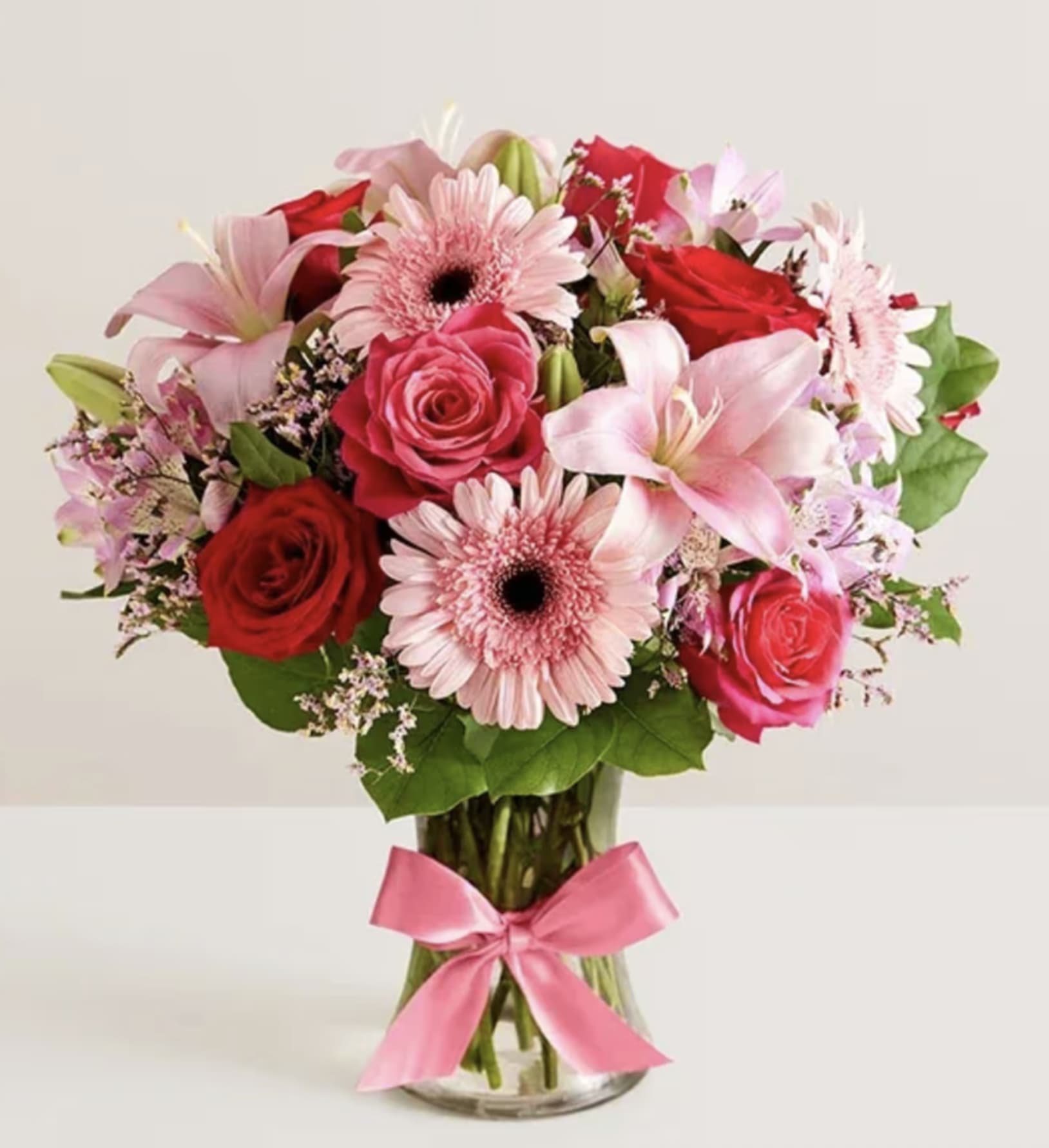 Bouquet of pink and red flowers in a clear glass vase with a pink ribbon