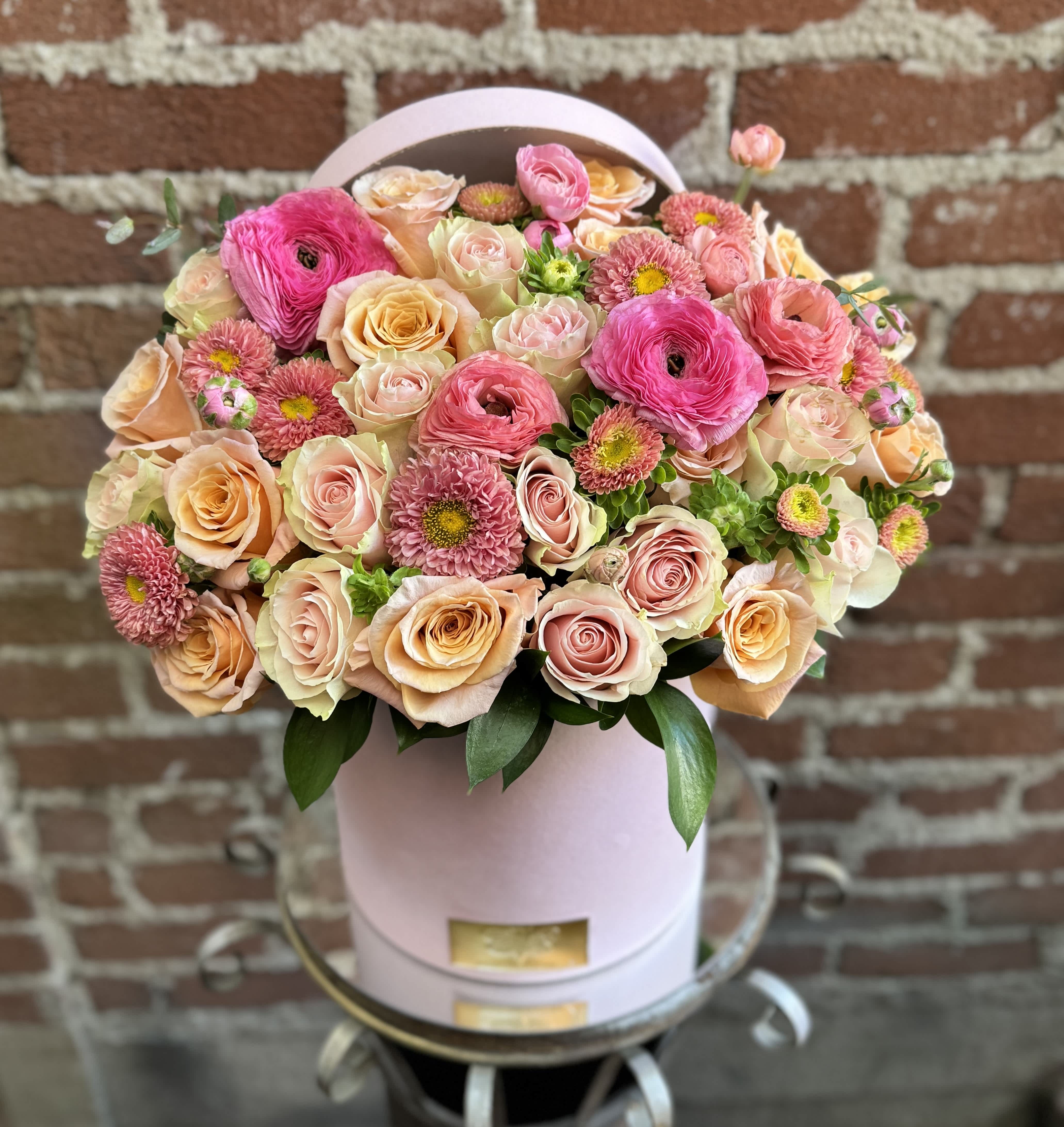 Pink and peach roses with small pink blooms in a round hatbox