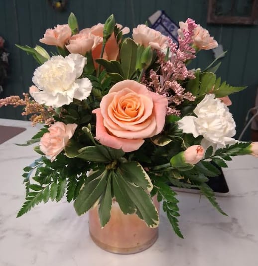 Peaches and Cream - Peaches &amp; Cream is a soft and elegant floral arrangement designed in a low peach cylinder vase, overflowing with creamy white blooms, delicate peach blossoms, and lush seasonal greens. Its warm pastel palette creates a fresh, graceful look that feels both timeless and inviting. Perfect for celebrating life’s sweetest moments, sending love, or adding a touch of gentle beauty to any space.