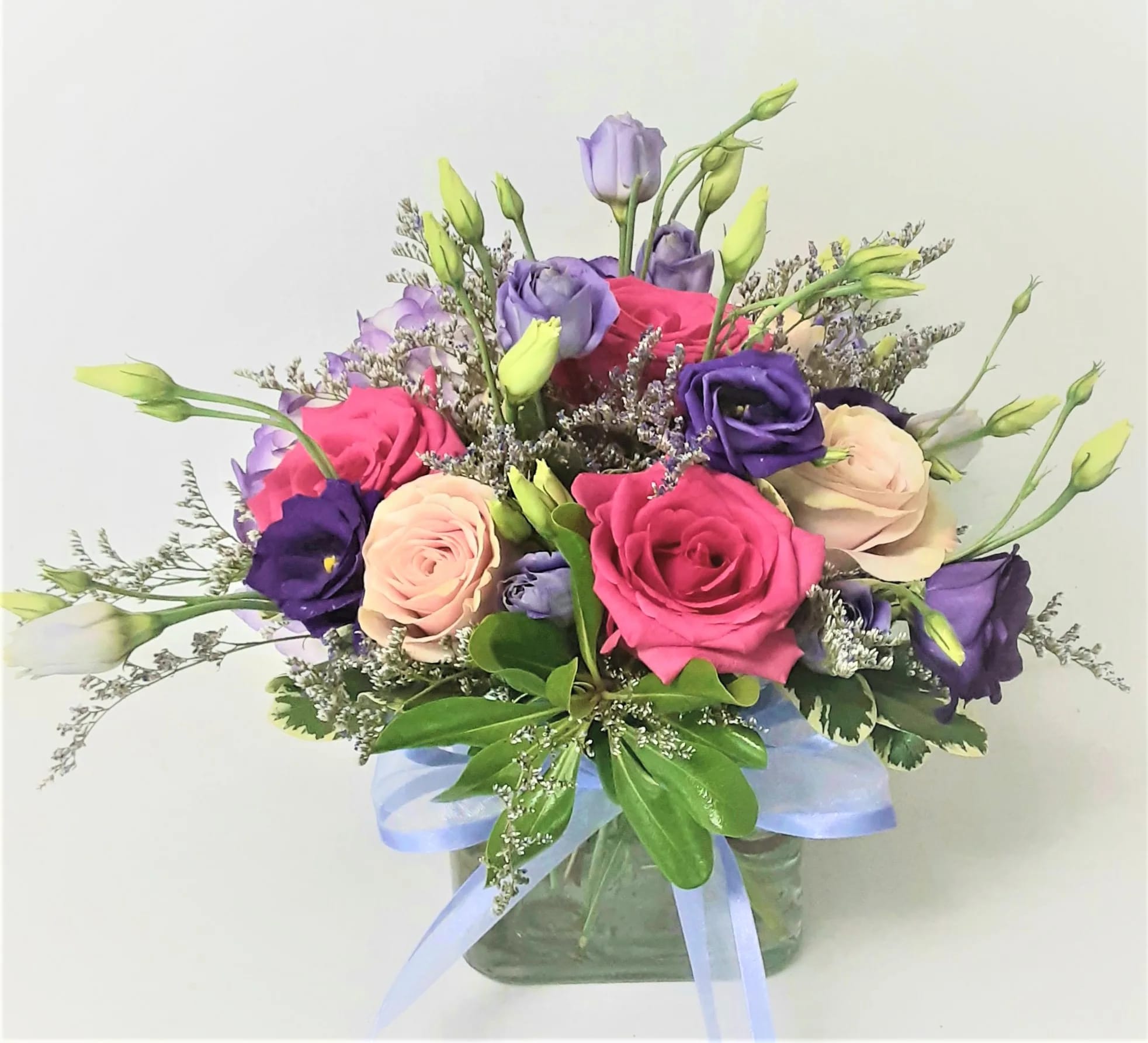 Pink, purple, and cream flowers in a glass vase with a blue ribbon