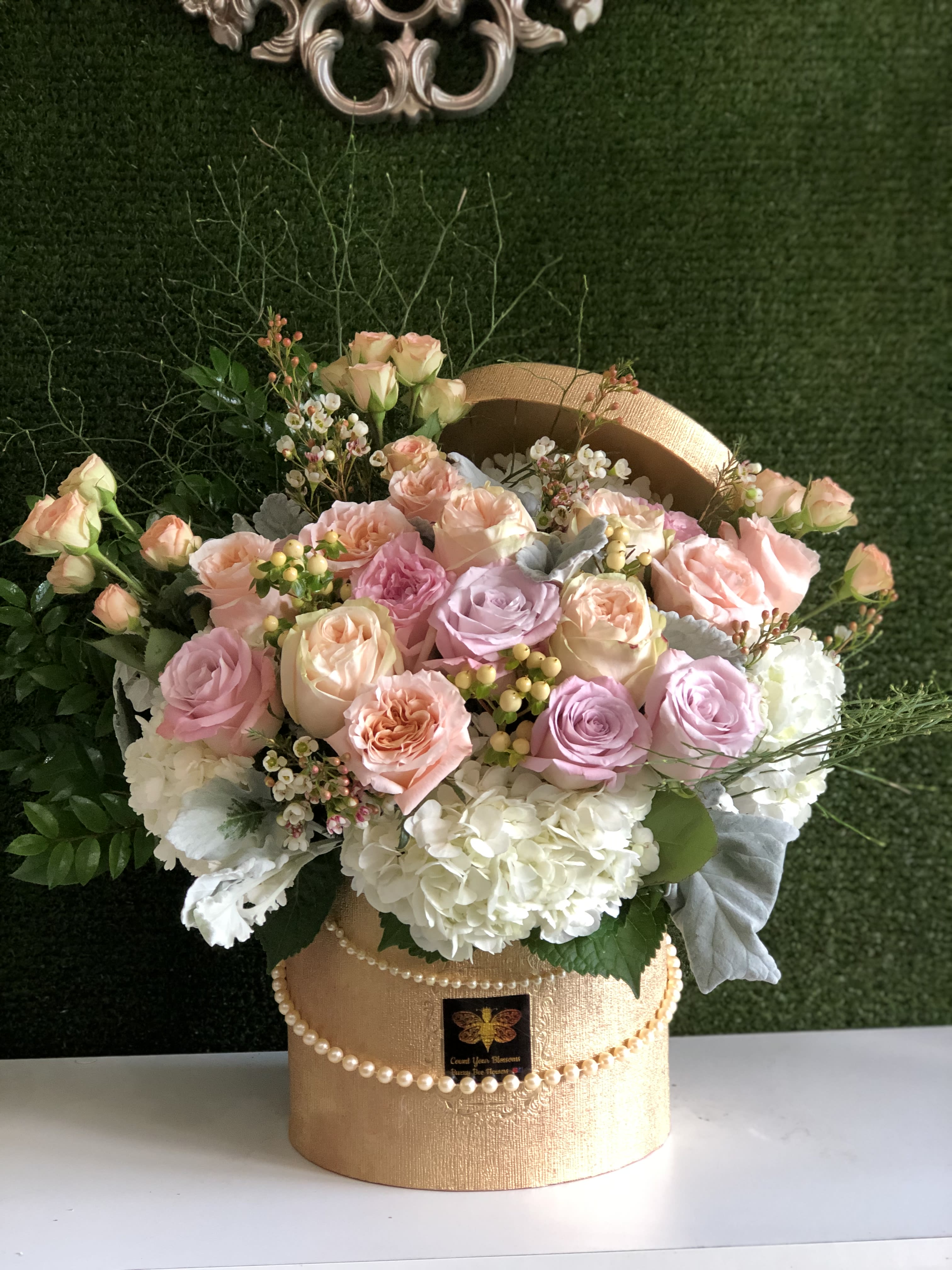 Pastel roses and white hydrangeas arranged in a gold hatbox