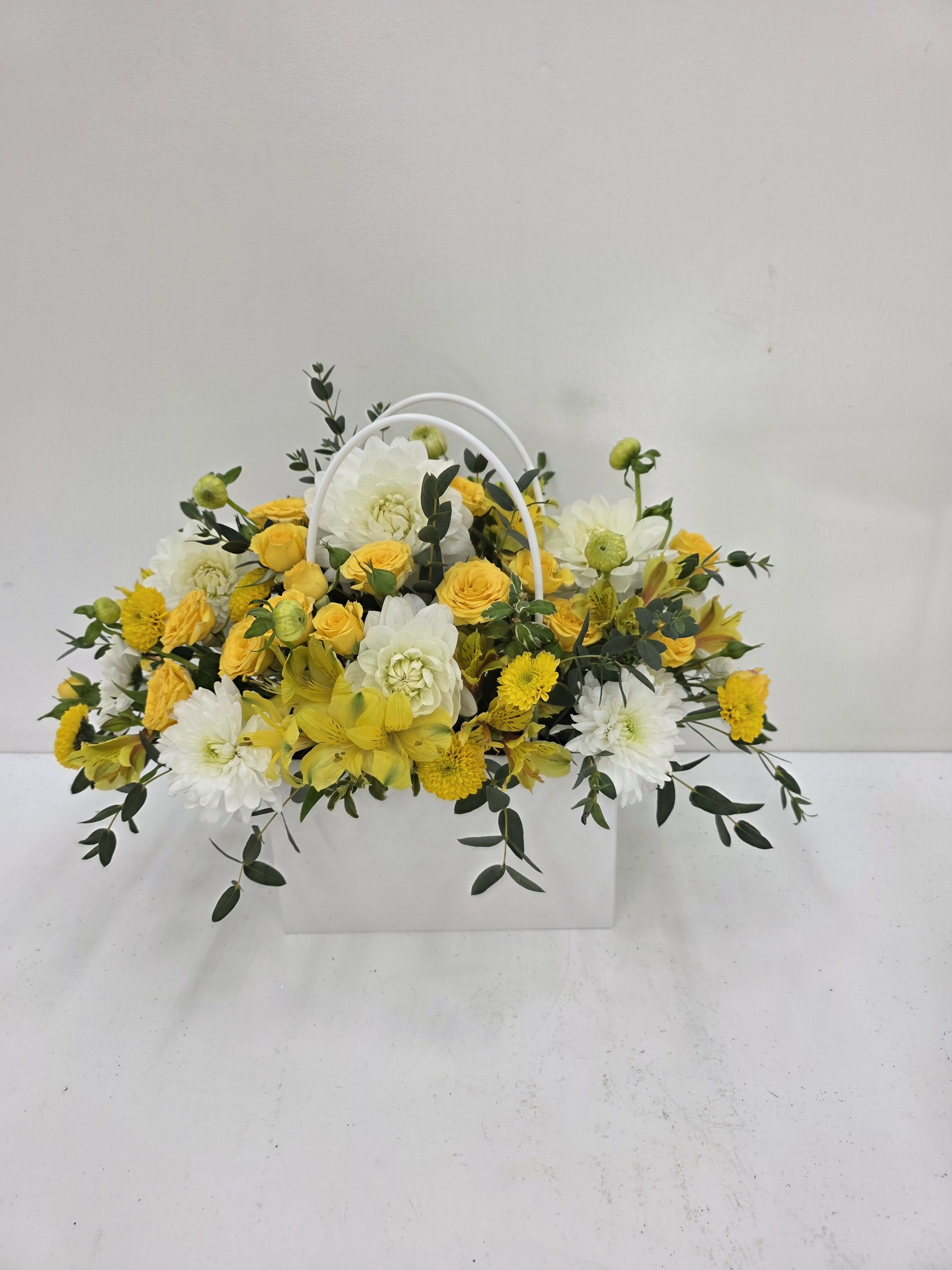 A Bag of Yellow Blooms - A bright mix of yellow spray roses and white chrysanthemums, and alstroemeria , accented by wisps of eucalyptus in a white handled bag. 